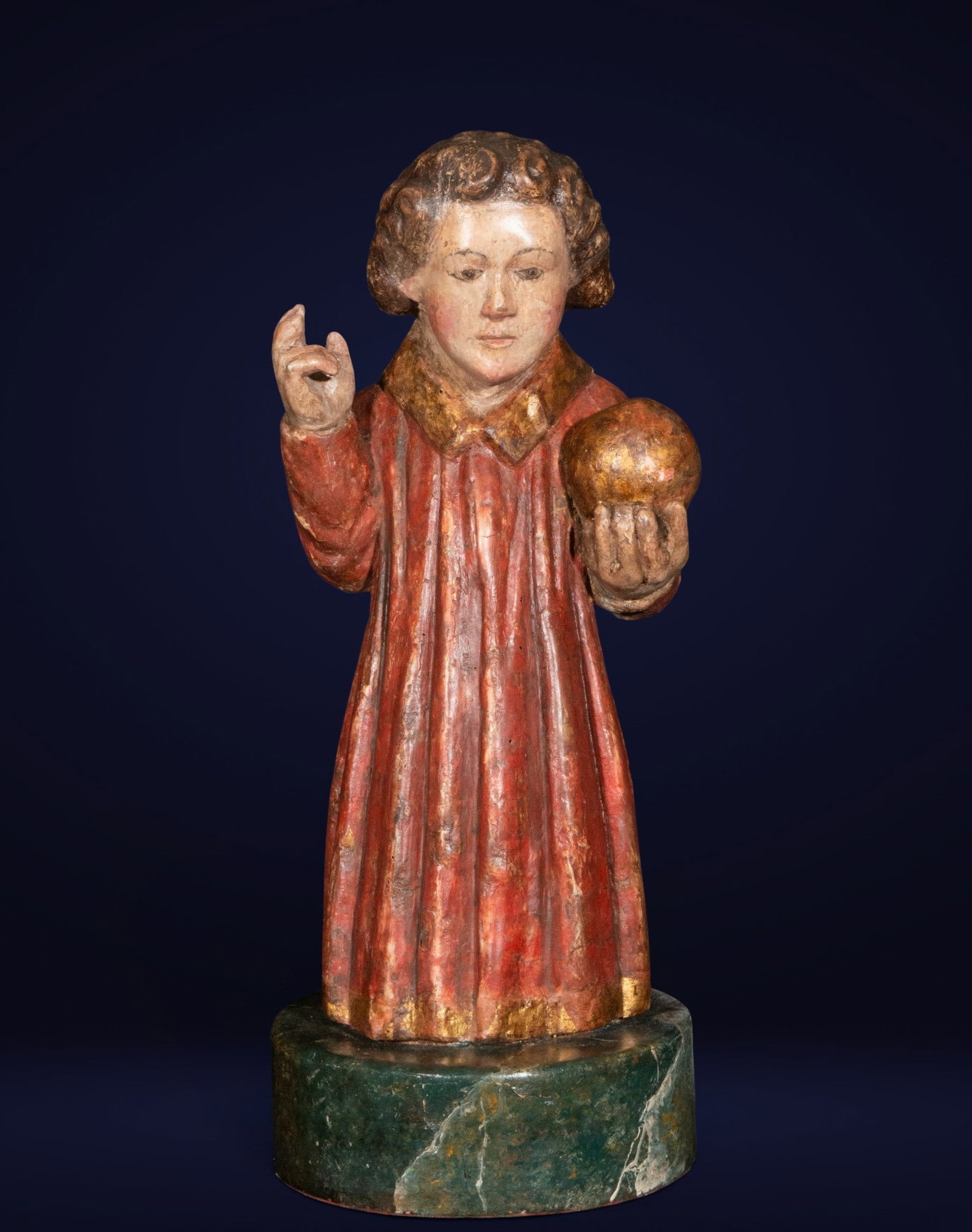 Boy with a Ball, Spanish Baroque School, 18th Century: Polychrome and gilded wood carving. Measures 37 x 17 x 16 cm. This devotional sculpture depicts the Christ Child standing, holding the orb of the world, his hand raised in a gesture of blessing. The f