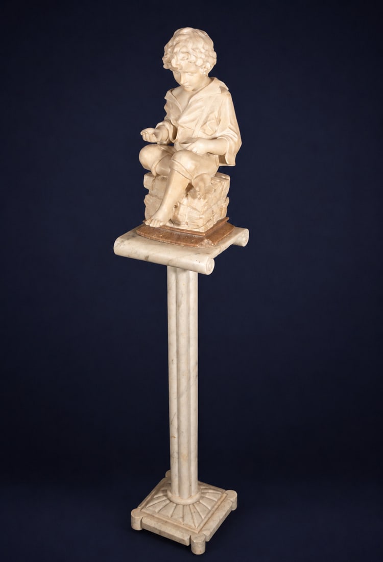 Child seated on a pedestal, French Academic School, 19th - 20th Century: Carved marble. Measures 143 x 26 x 26 cm. This sculpture in the round depicts a young boy seated on a rocky base, absorbed in contemplation of a small object held in his hand. The composition conveys 