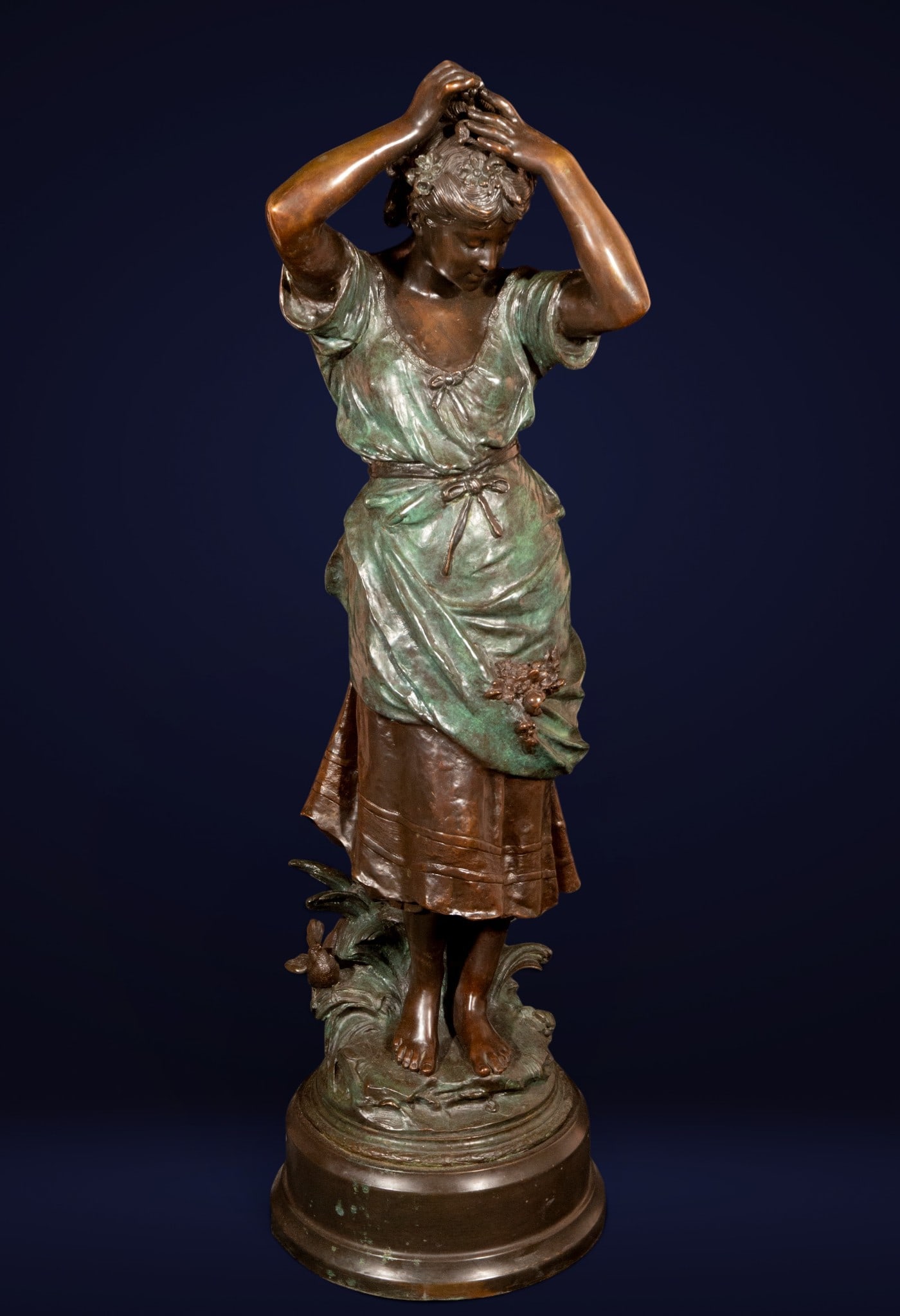 Young woman with floral crown, French Art Nouveau School, 19th-20th century: Patinated and partially polychromed bronze. Measures 104 x 32 x 30 cm. This female sculpture, with its distinctly Symbolist sensibility, depicts a young woman in an introspective pose, weaving a crown