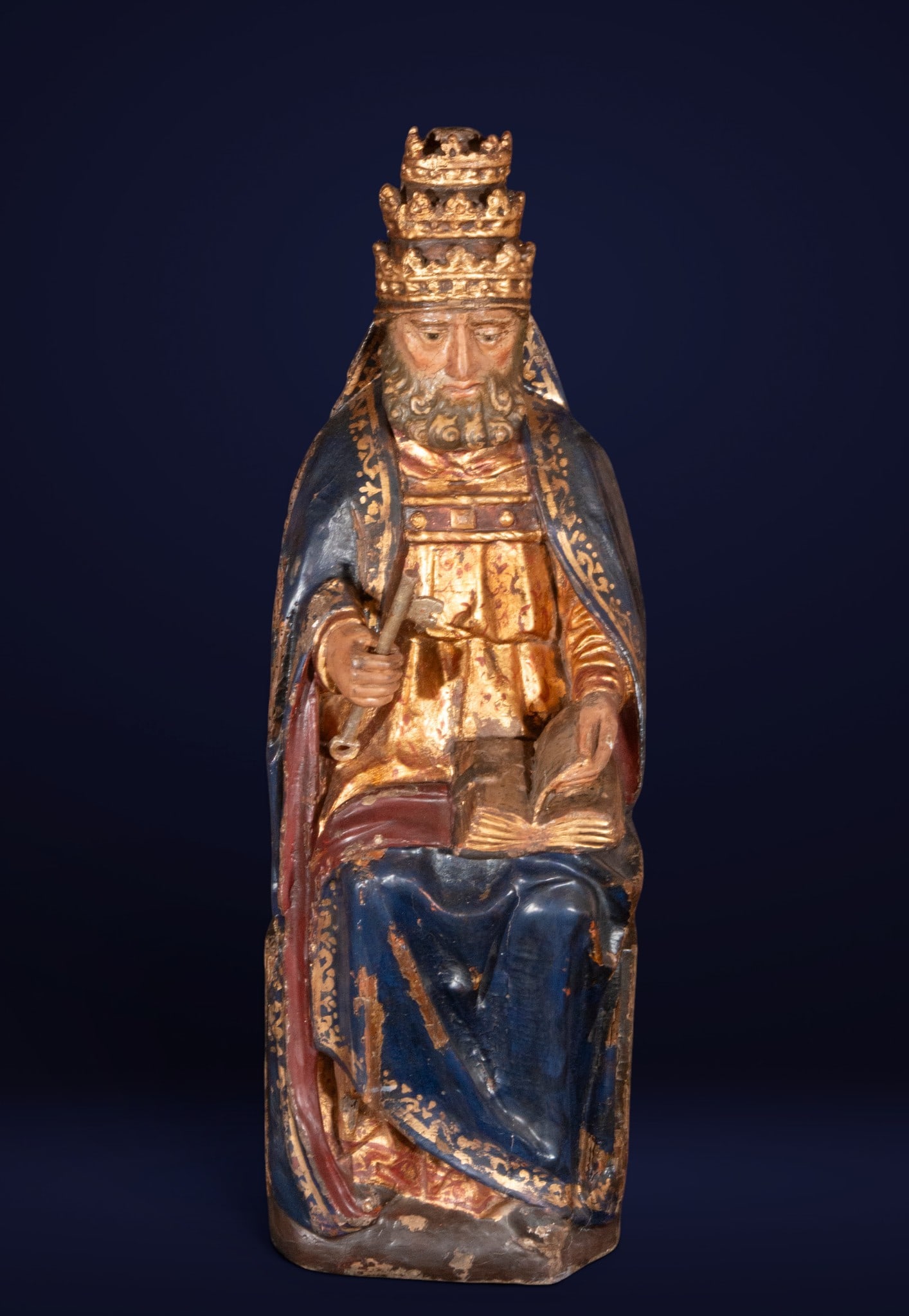 King enthroned with book and key, Castilian School, 16th Century: Carved, polychromed, and gilded wood. Dimensions: 68 x 23 cm. This sculpture in the round depicts a seated royal figure on a throne, identified by the presence of a large key and an open book, attribu