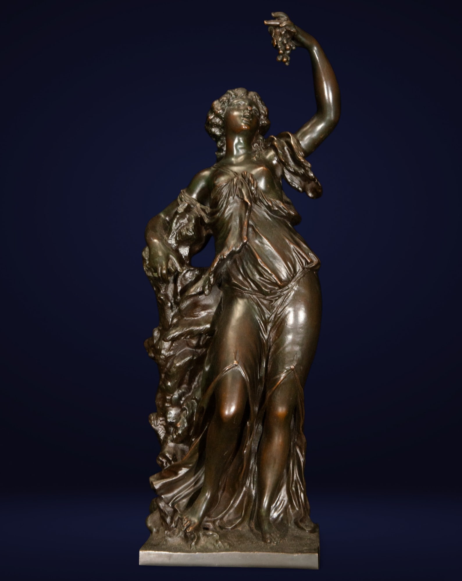 Figure of a woman with grapes, "The Grape Harvest." Italian School. 19th century.: Patinated bronze. Allegorical sculpture depicting a female figure holding a bunch of grapes, a symbol of abundance and the wine-growing cycle. The naturalistic treatment of the anatomy and the elegant