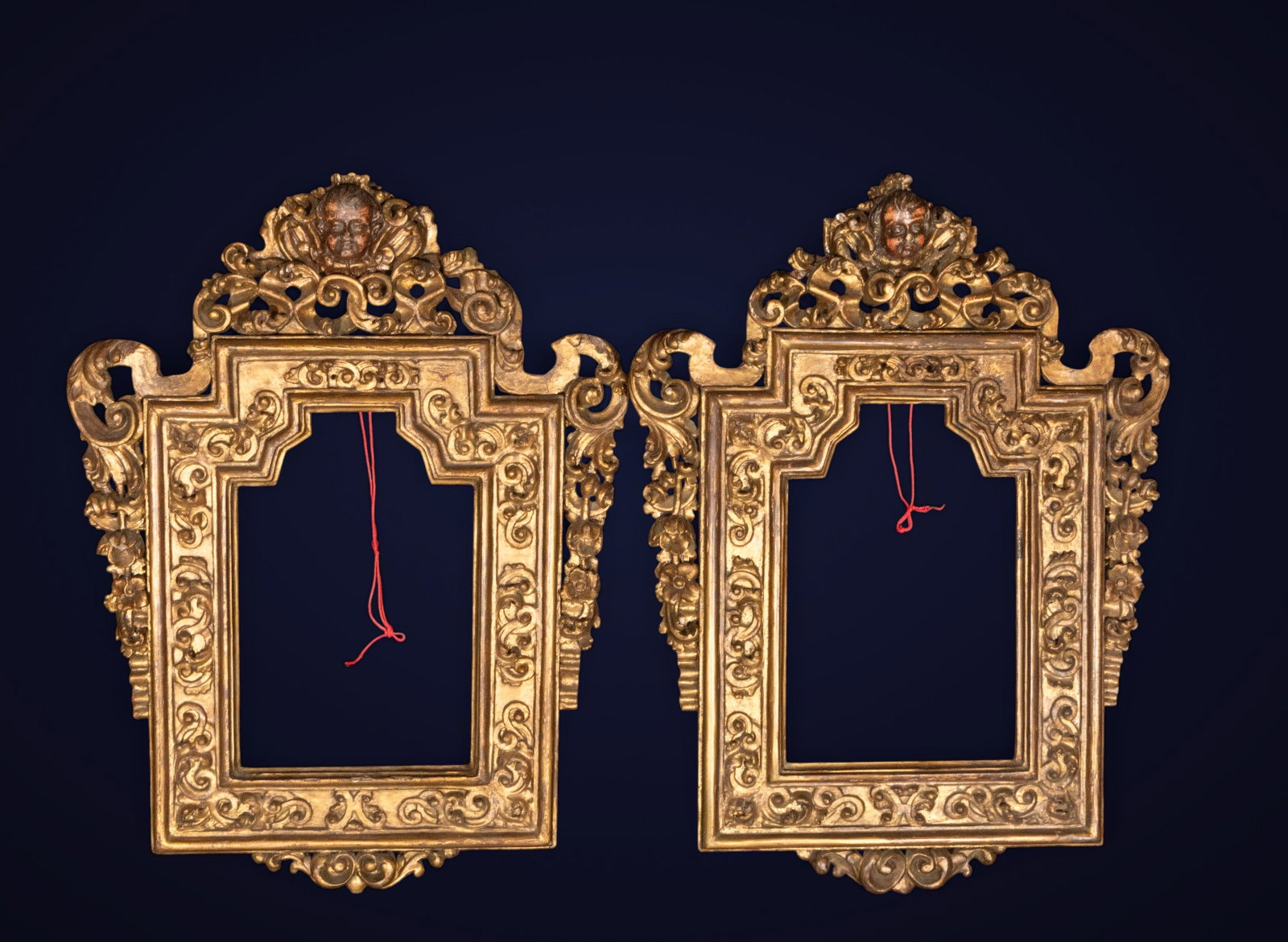 Pair of Baroque mirror frames, Spanish school, 17th century: Carved and gilded wood. Dimensions: 43 x 28 cm; 82 x 62 cm. Pair of mirror frames with an architectural profile, richly carved with scrolls, leaves, and a top finial adorned with cherub heads. The sil