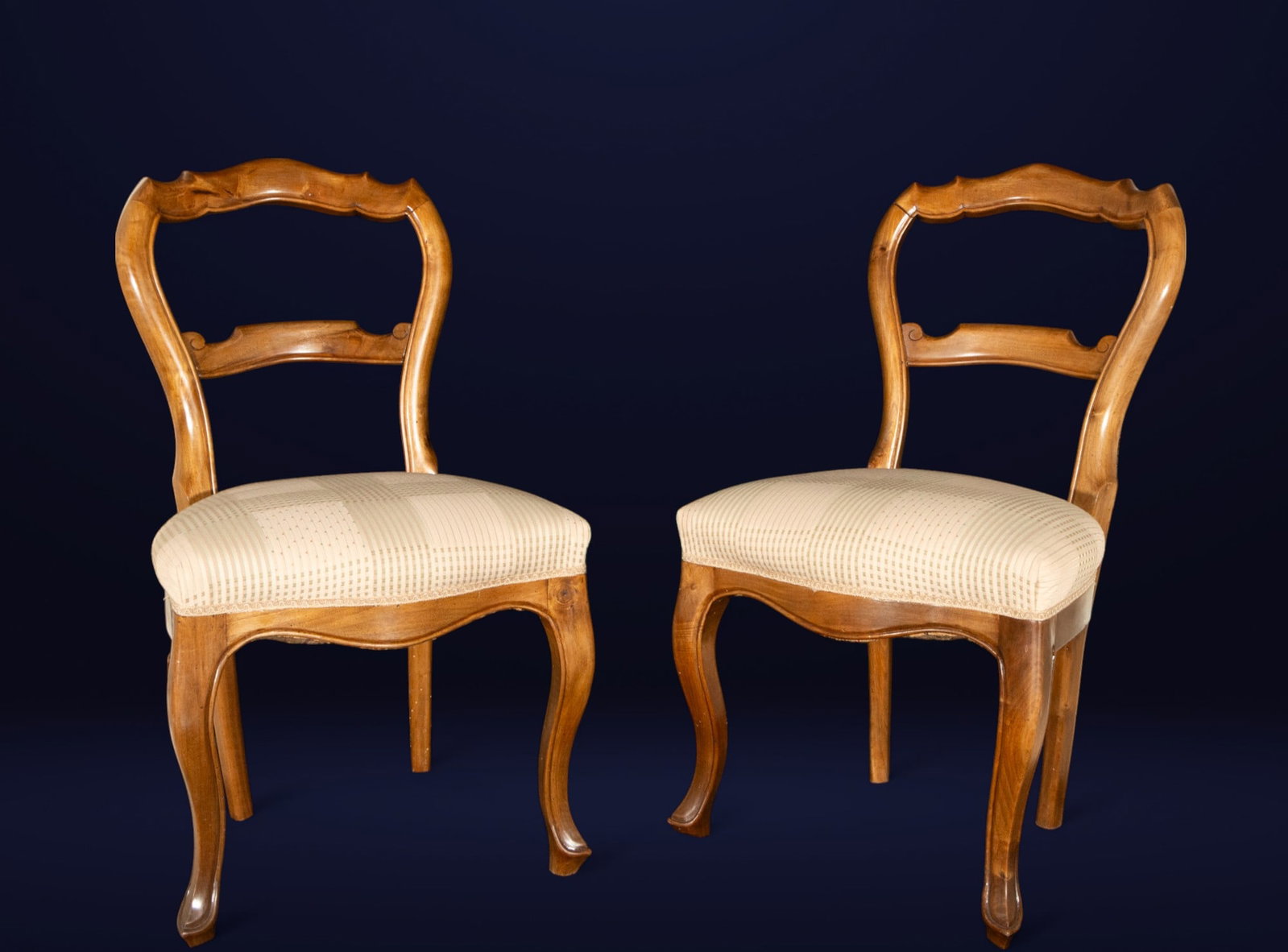 Pair of Elizabethan chairs. Spanish School. 19th century: Pair of Elizabethan chairs in carved wood, featuring an open back with a molded double crossbar and a sinuous contour framing a decorative profile inspired by Rococo. The seat, upholstered in beige fa