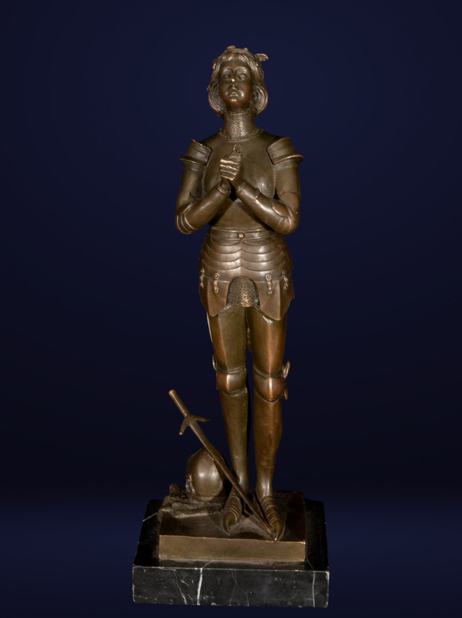 Joan of Arc. Signed. French School. 20th Century: Patinated bronze. Measures 51 x 18 x 13 cm. Sculpture of Joan of Arc depicted in prayer, dressed in armor and accompanied by a helmet and sword. The figure features a balanced vertical composition and
