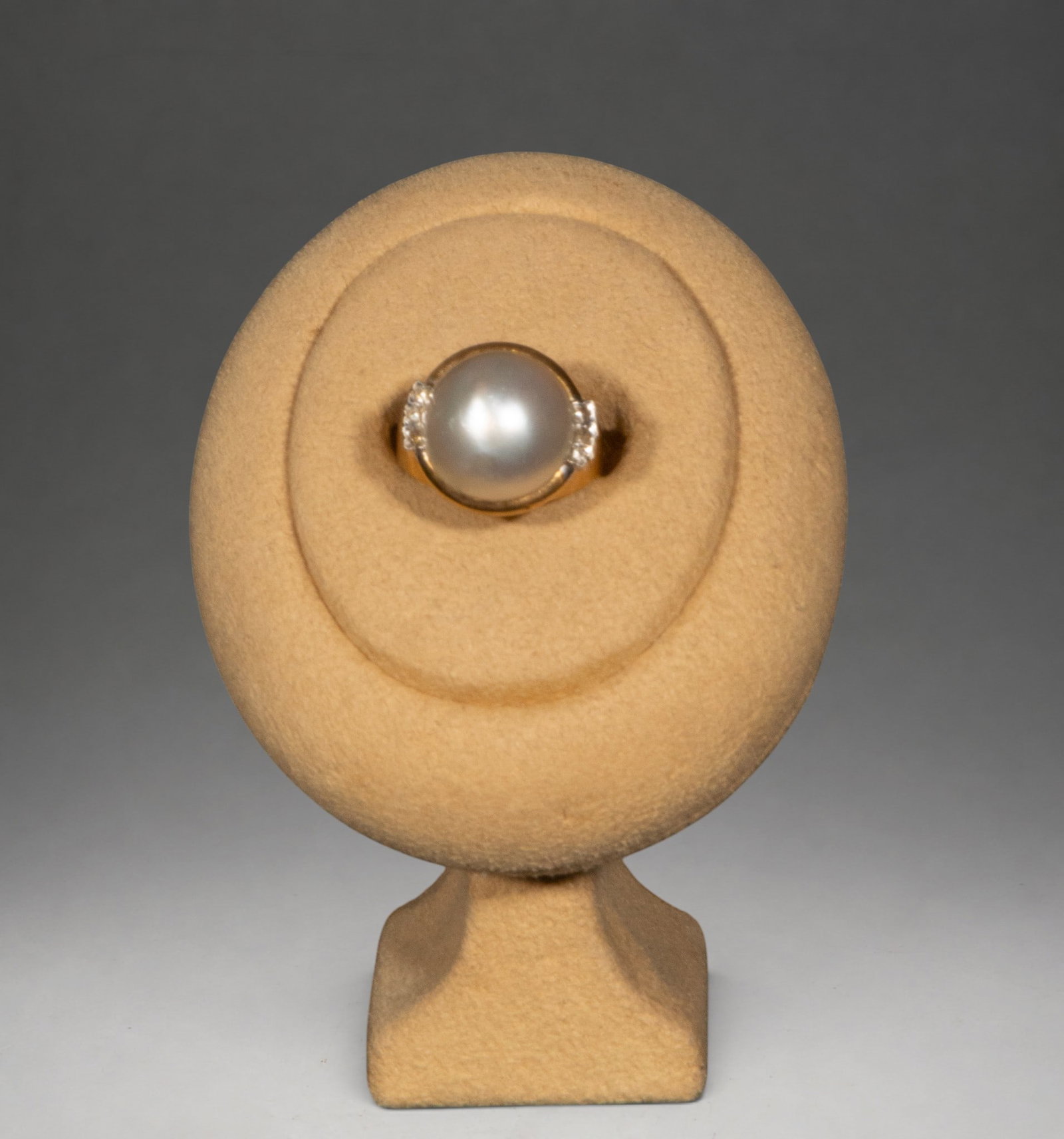 18K gold pearl and diamond ring: 6g. Ring crafted in 18k gold with a central, rounded pearl set in a plain mount, flanked by two clusters of brilliant-cut diamonds on either side that add luminosity and enhance the piece. It features