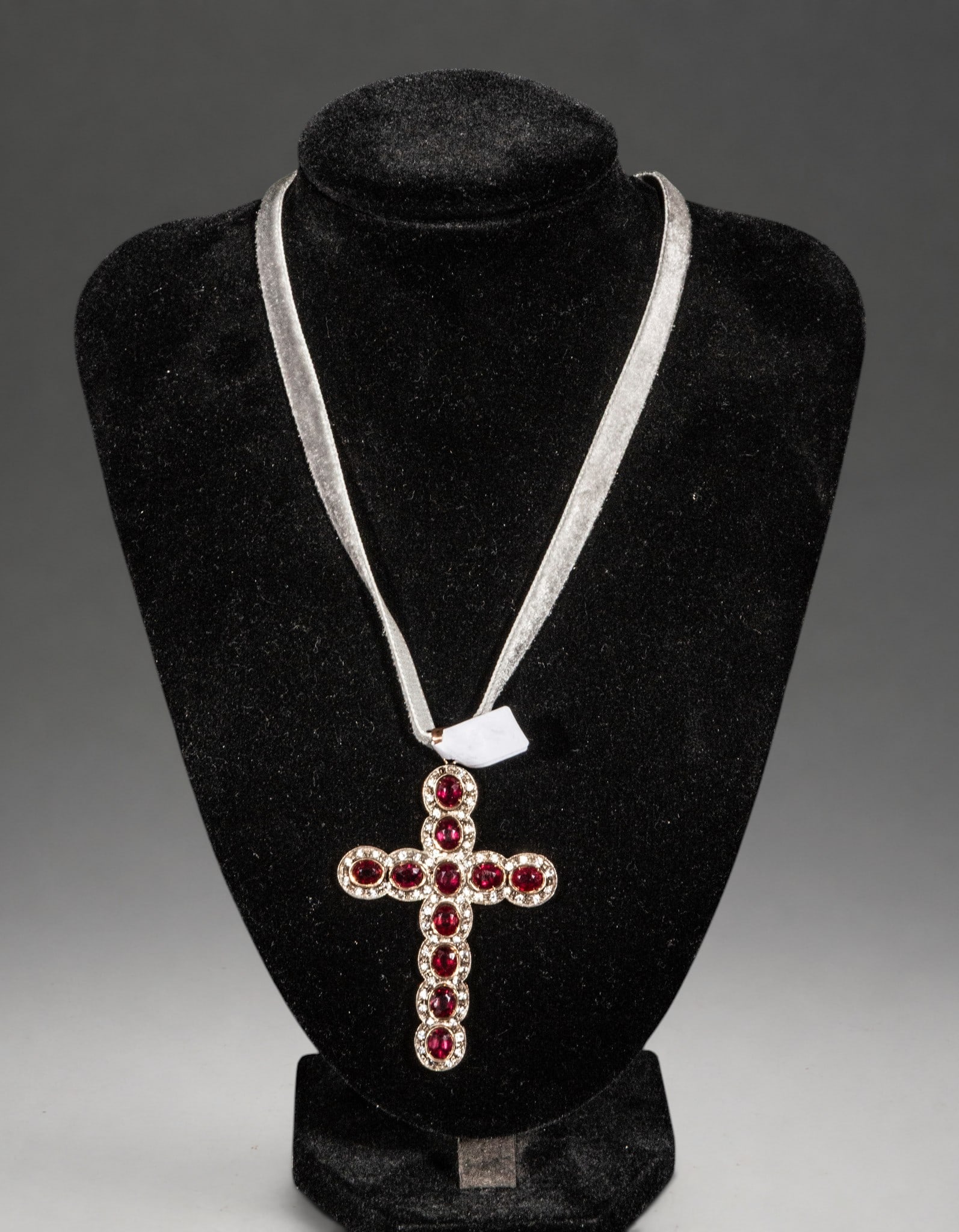 18k Gold and silver cross with garnets and diamonds: A cross-shaped pendant crafted in gold and silver, adorned with oval cabochons of deep red garnet surrounded by halos of small diamonds. The symmetrical composition enhances the symbolism of the cross