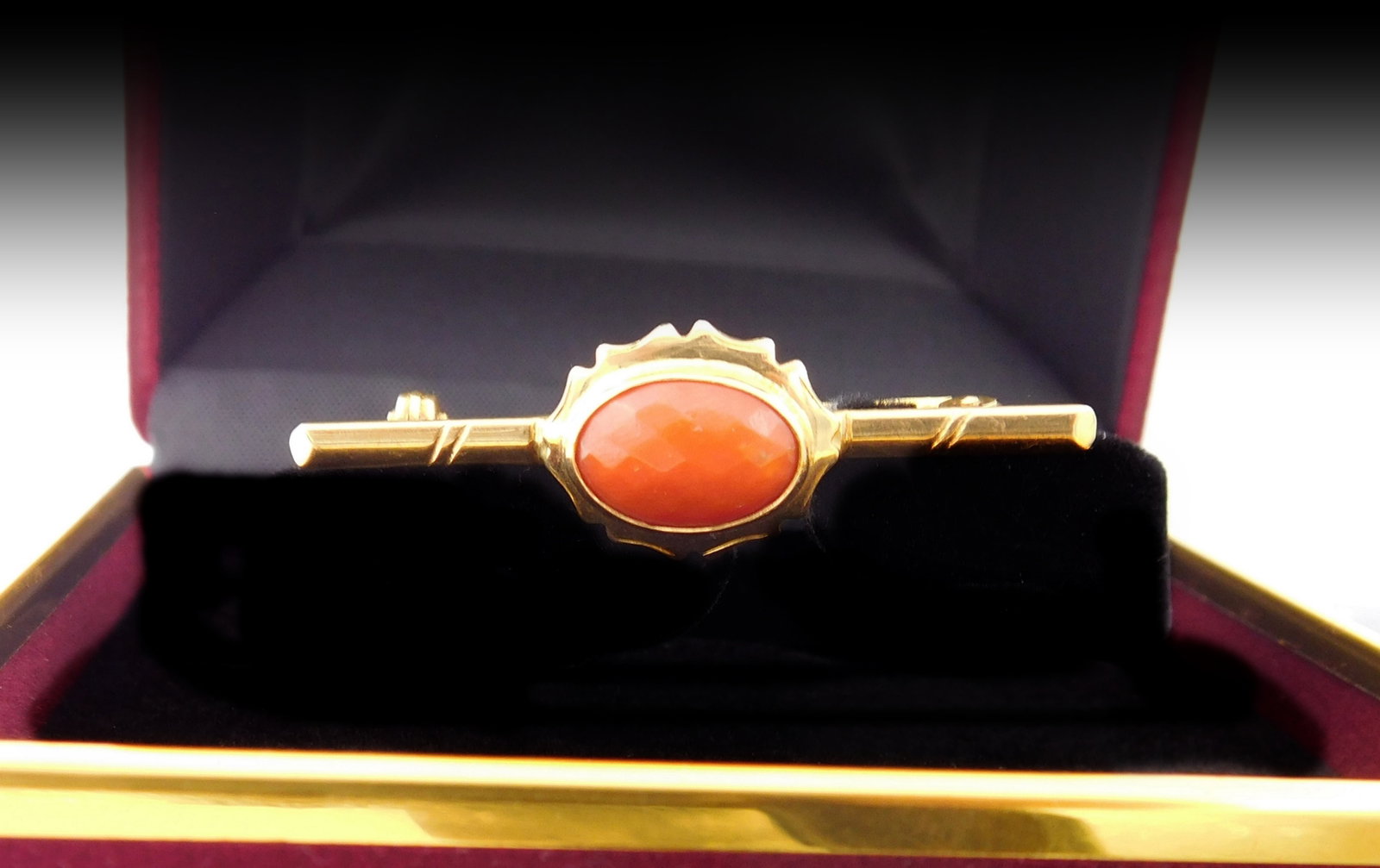 Vintage 18k gold brooch with natural red coral, Weight: 5.8 gr. Italian, 20th century: Delicate vintage brooch with a small, elongated structure, crafted in bright 18-karat yellow gold, featuring a natural red coral oval cabochon (15 x 10 mm) set in a bezel within a mount with a serrate
