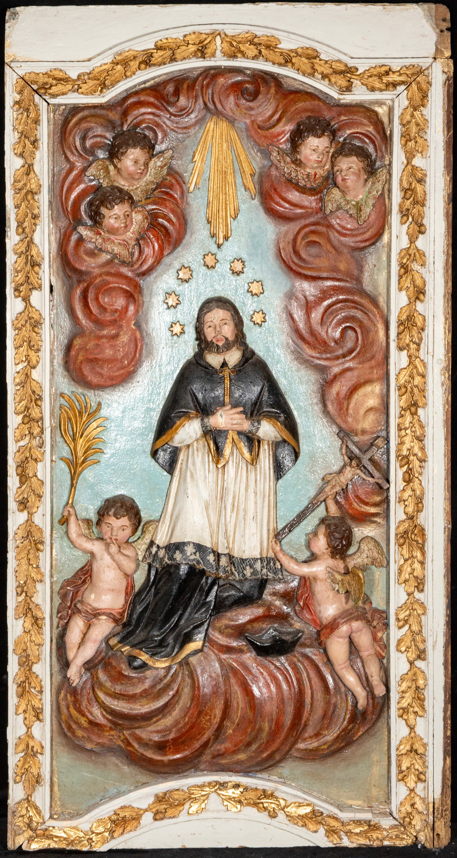 Relief of a Dominican saint. Colonial school. 18th century: Polychrome wood relief. Measures 106 × 55 cm. Image of a Dominican saint surrounded by cherubs and rays of light, carved with remarkable volume and rich polychromy, an example of 18th-century colonia
