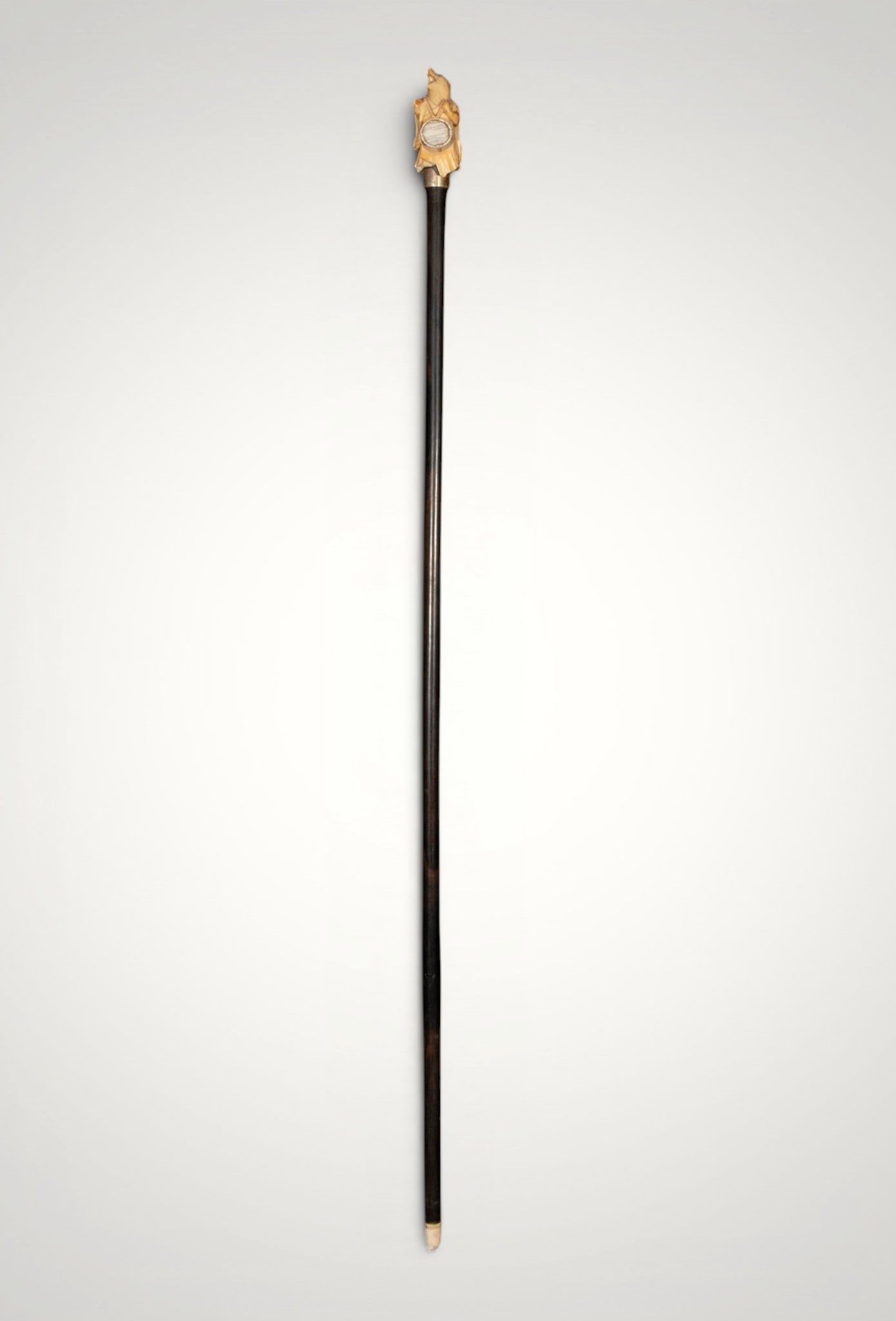 Zoomorphic musician's staff with netsuke. Japanese School. 19th Century: Polished ebony wood, carved in fine material, and mounted on a metal. Measures 90 x 4 cm. This small walking stick is topped with a Japanese netsuke carved as a zoomorphic figure dressed in a flowing 