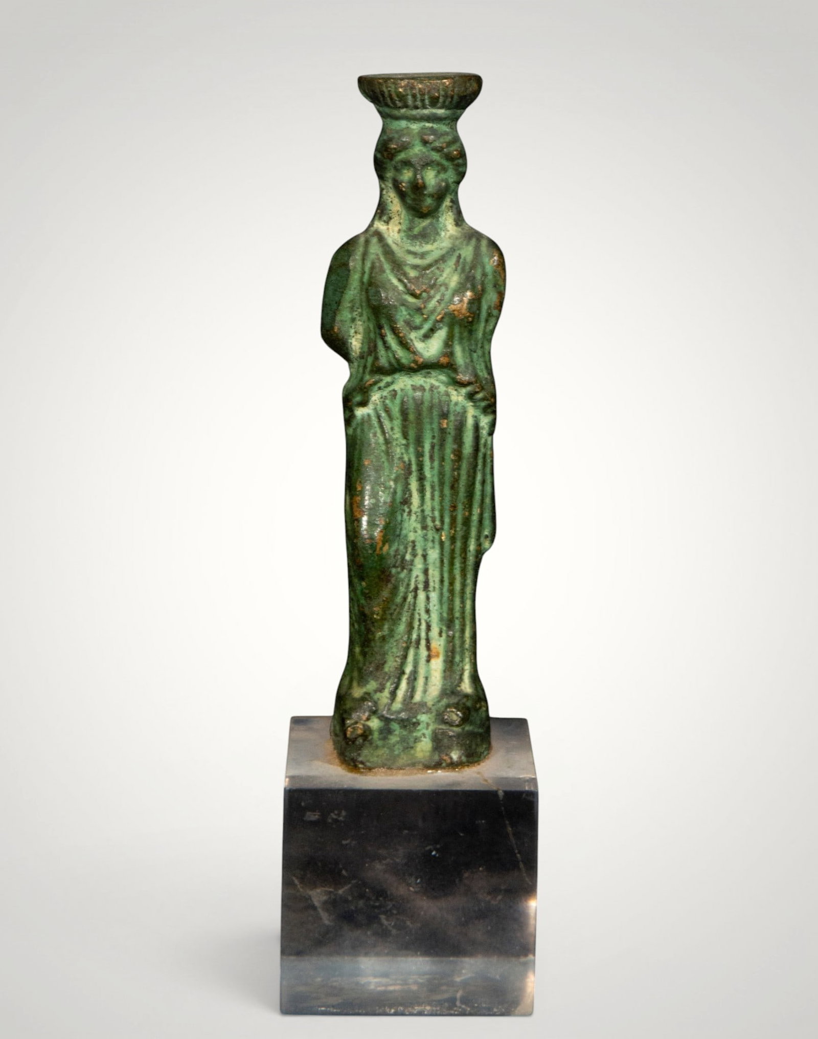 Seated goddess with headdress. Grand Tour style. Italian school. 19th century: Cast bronze, chiseled and patinated on a marble base. Base measures 12 x 25.5 cm; figure 9 x 2.5 cm. Seated female figure, adorned with a long tunic with vertical folds and an elevated headdress, conc