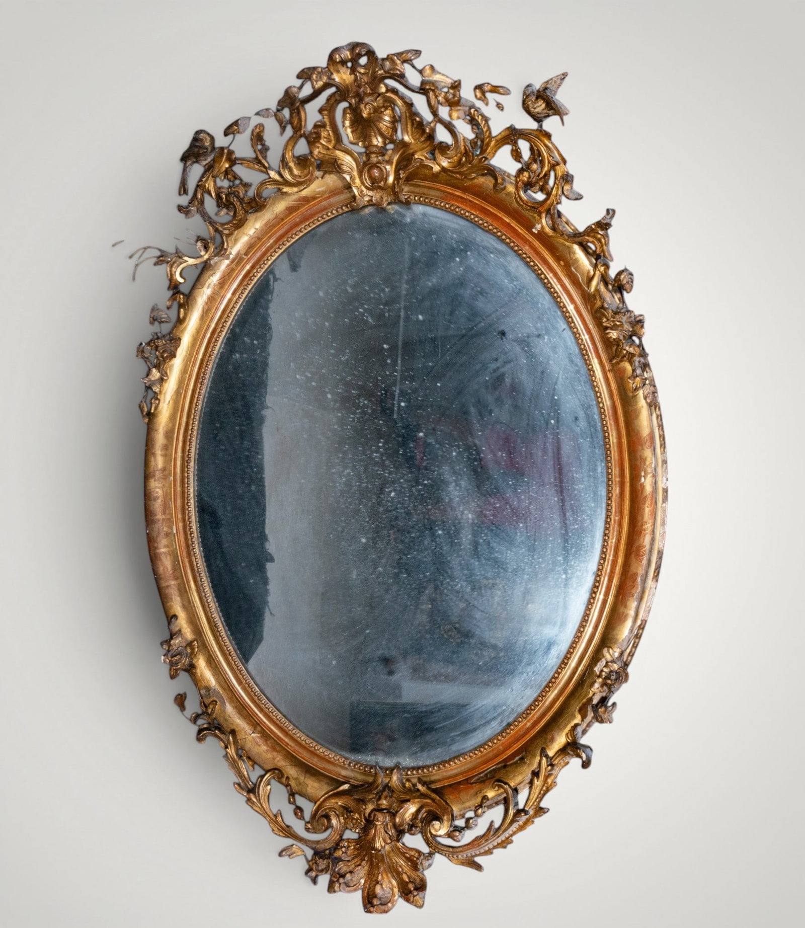 Oval mirror with Rococo cresting. European School. 19th century: Carved and gilded wood with mirror. Measures 123 x 95 cm - 174 x 116 cm. Large oval mirror with openwork cresting of scrolls, flowers, and birds, extending into a lower finial of leaves and volutes. T