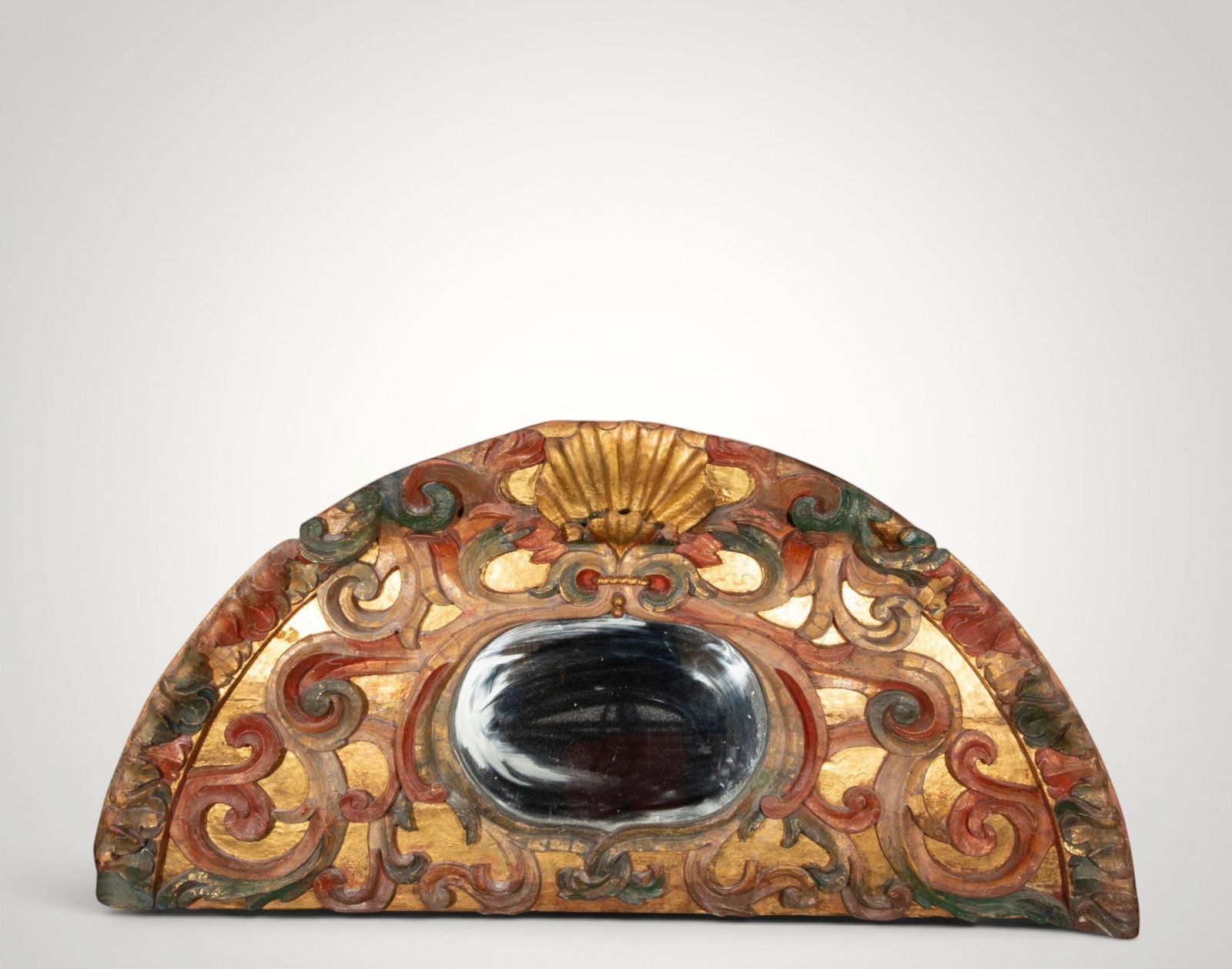 Ornamental finial with oval mirror. Hispanic School. 18th century: Carved, polychromed, and gilded wood with a mirror. Measures 85 x 173 cm. Semicircular element with a small central oval moon, surrounded by scrolls, leaves, and a large shell at the top. The red and 