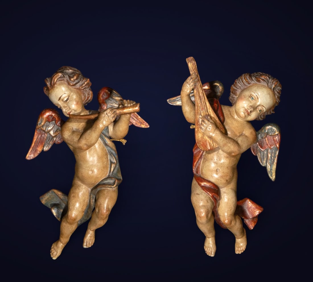 Pair of little angels, European School, Late 18th - 19th Century: Carved and polychromed wood. Measures 23 x 30 x 10 cm. A pair of child-like angels depicted in dynamic poses, one playing a flute and the other a string, with outstretched wings and slightly twisted b