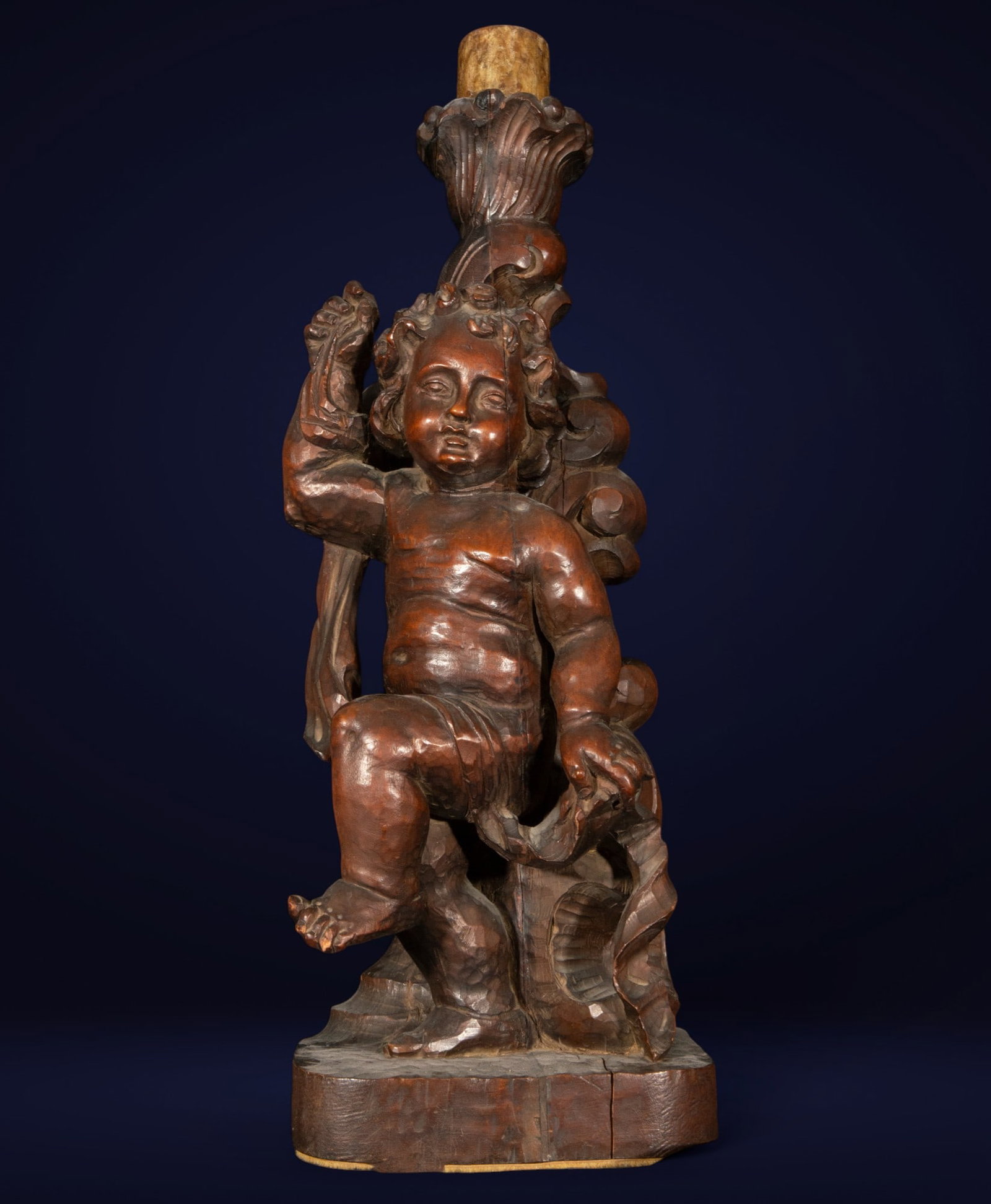 Sculpture of a torch-bearing angel. Spanish Baroque School. 18th century.: A wood carving preserved in its original color. The figure of a torch-bearing angel unfolds with expressive tenderness in its rounded anatomy and serene face. Standing on a faceted base, the child hol