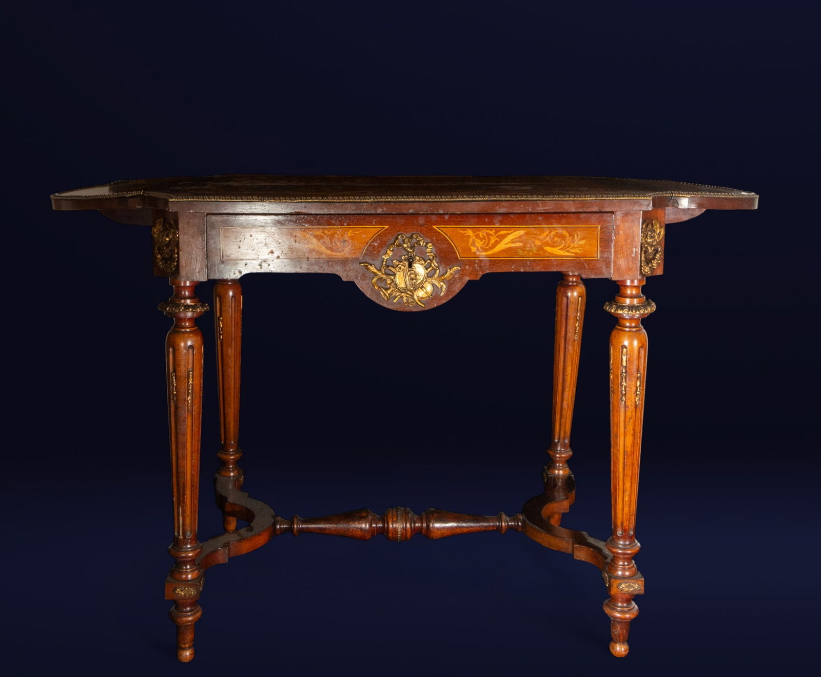 Table with marquetry and gilt bronze mounts. French School. 19th century: Mahogany and rosewood with marquetry and gilt bronze details. Dimensions: 77 x 120 x 65 cm. Rectangular table with an elegant structure, featuring a contoured top and fluted legs joined by a turned ce