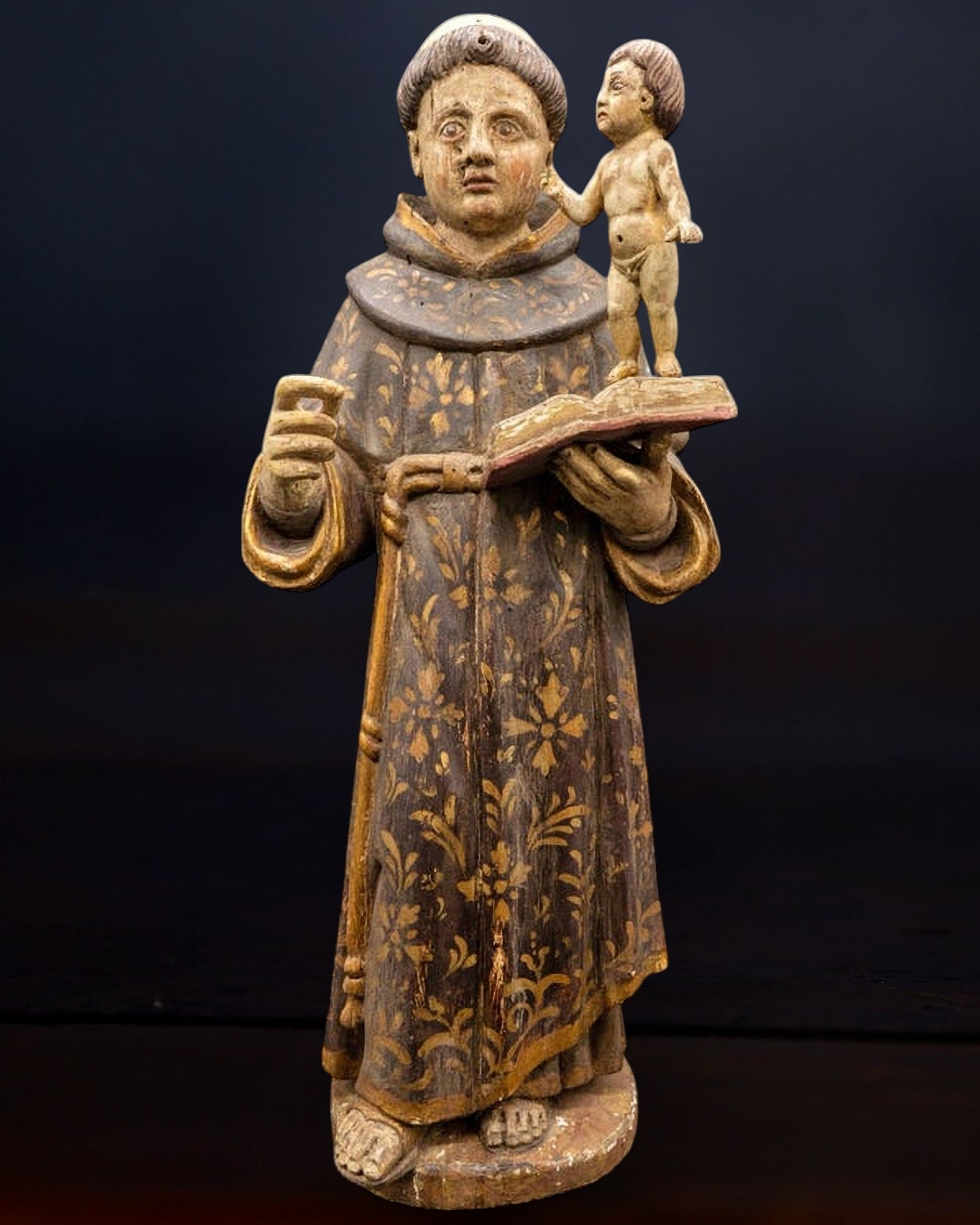 St. Anthony and the Child Jesus, Portuguese colonial school in Goa, 17th century: Polychrome and gilded wood. A devotional sculpture in the round depicting Saint Anthony of Padua in a frontal position, holding an open book in his left hand, over which stands the infant figure of th
