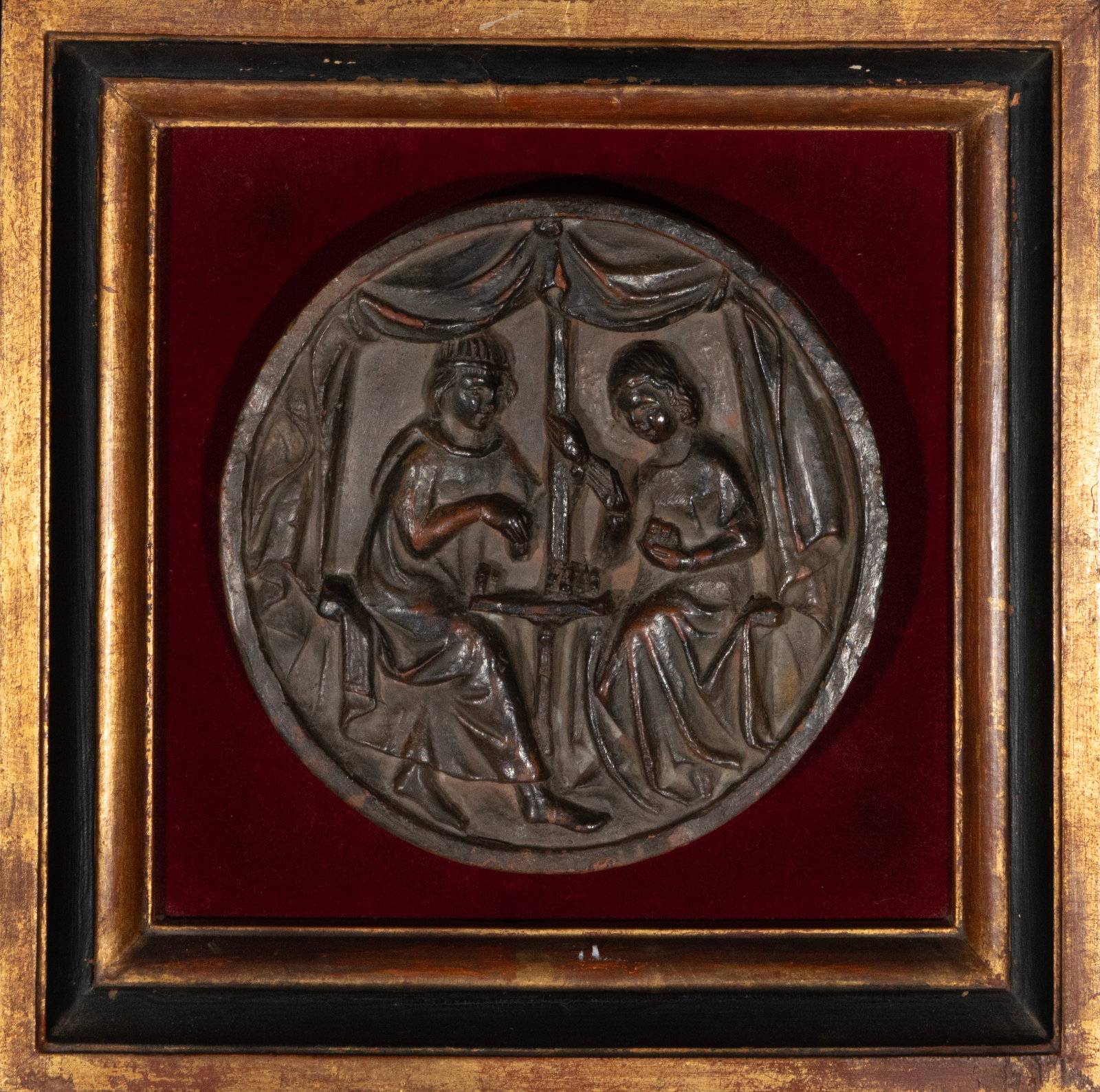 Circular relief in medieval style made of terracotta: Terracotta relief. Measures 21 x 20 cm; with frame 34 x 32 cm. Circular interior scene with two figures seated facing each other under a raised canopy. A small central table is placed between them, wh