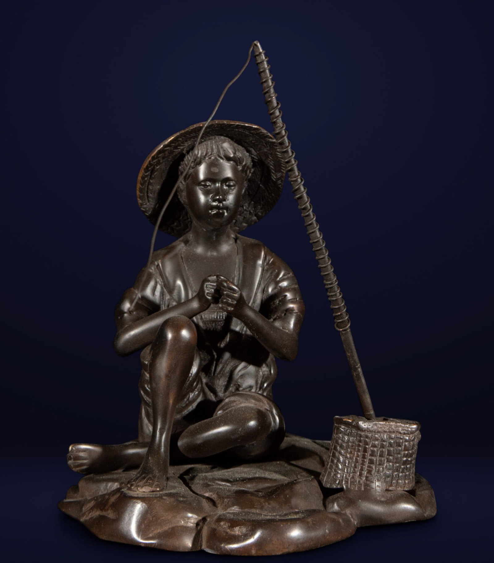 Asian Fisherman. Oriental School. 20th Century: Patinated bronze sculpture. A seated male figure of Asian origin, characterized by his ethnographic features, conical hat, and fishing rod. The piece captures a traditional scene with naturalism, high