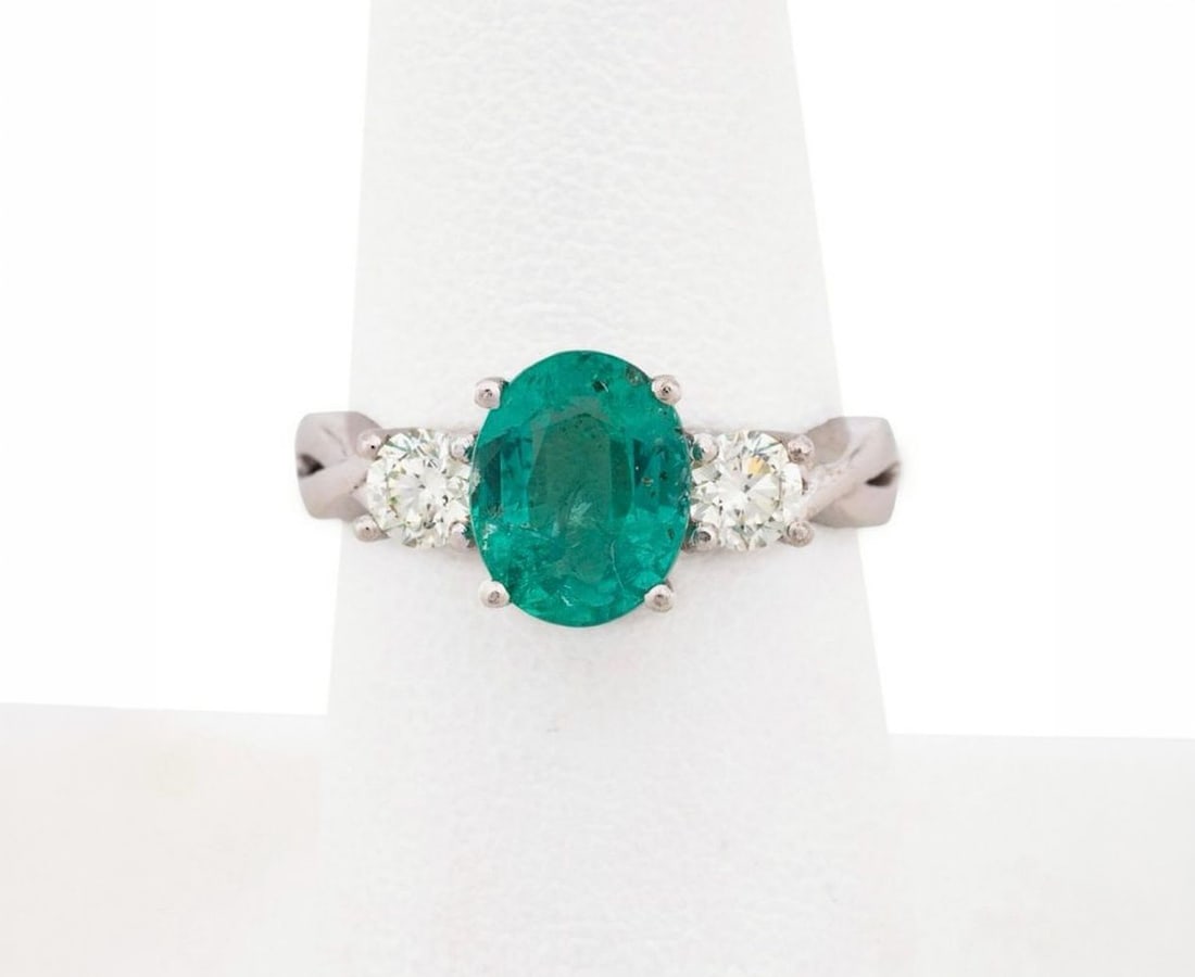 Gold ring with emerald and diamonds: This ring, crafted in 18-karat white gold and weighing approximately 4.00 g, features a natural emerald of approximately 2 ct, set in an oval cut. The central stone is flanked by two brilliant-cut (fu