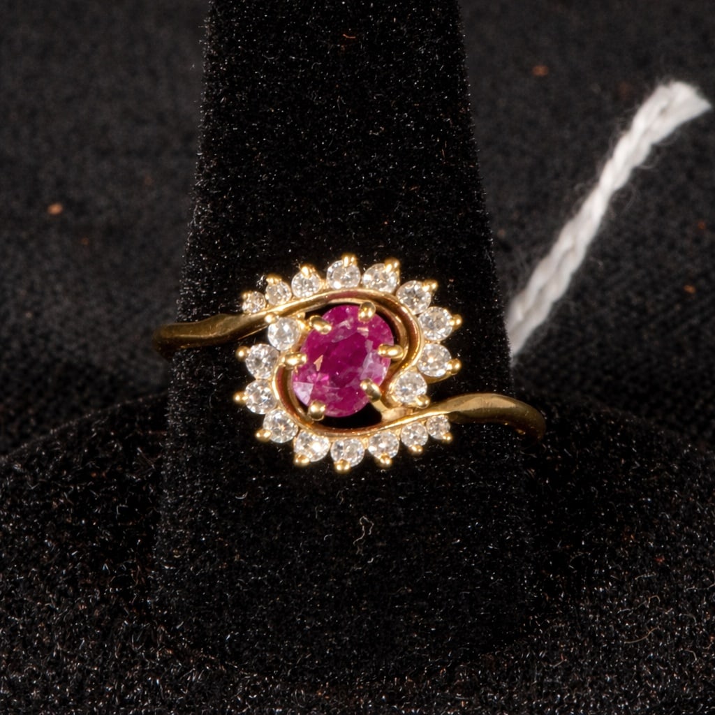 18k Gold ruby ??and diamond ring: 18k Gold, ruby, and diamond ring. Featuring a yellow gold band, the ring centers on an oval ruby ??surrounded by a halo of diamonds, creating a striking floral or rosette motif. The enveloping arrange