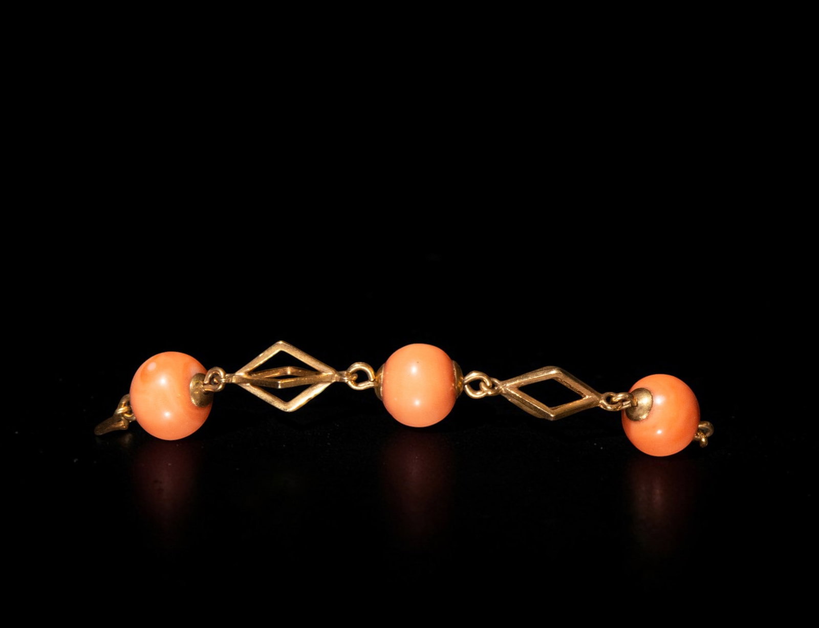 Yellow 18k gold bracelet and coral beads 18.98 grams: A bracelet in yellow 18k gold and coral beads, weighing 18.98 grams, composed of three pinkish-orange coral beads linked by openwork geometric motifs and metal connectors. The structure features a lig