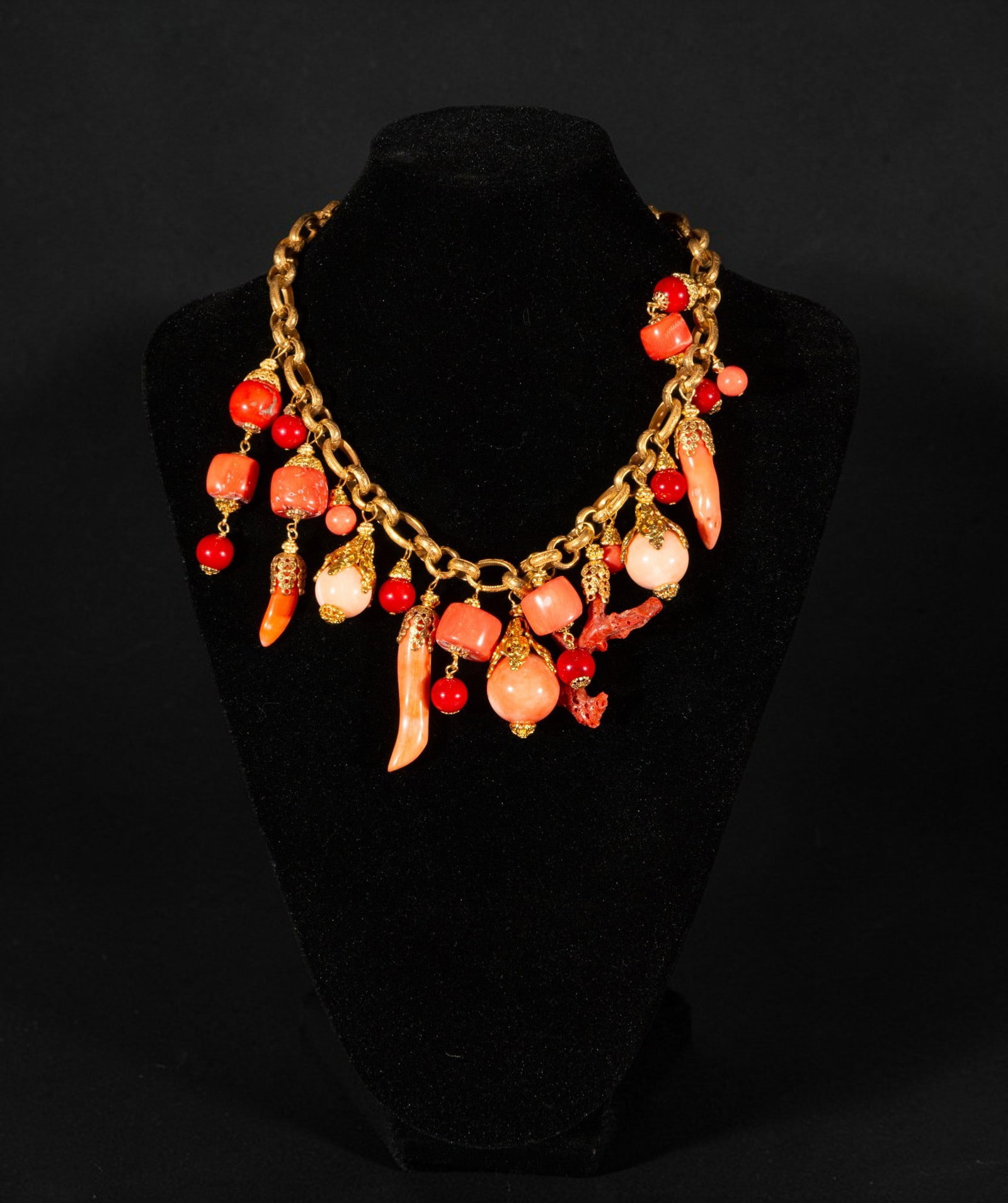 Gold-plated silver necklace with coral: Gold-plated silver necklace with coral. It features a large link chain from which multiple coral pieces in shades of red and pink are suspended, combined with pendants in spherical, cylindrical, scall