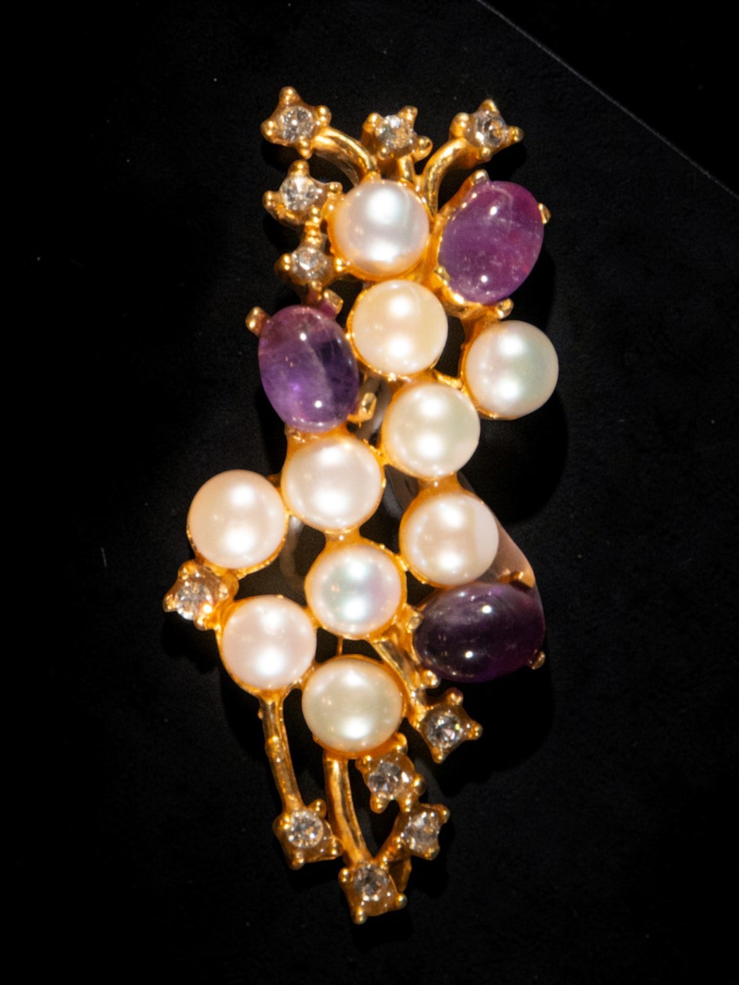 Gold-plated silver brooch with pearls and amethysts: A gilt-plated silver brooch with pearls and amethysts. The design unfolds vertically within a sinuous gilt metal structure, adorned with rounded pearls and oval amethyst cabochons, complemented by sma