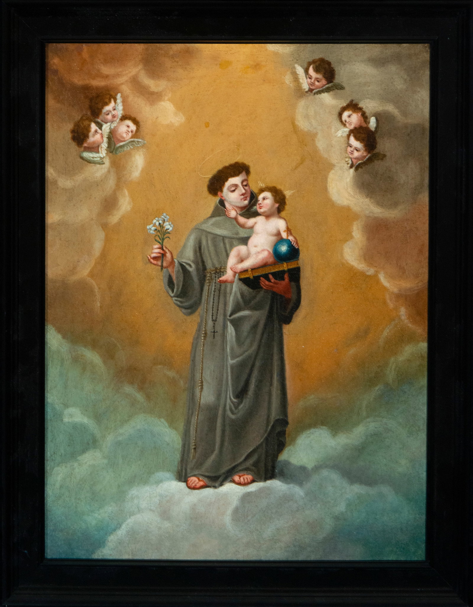 Saint Anthony of Padua with the Child Jesus. Cuzco School. 18th Century.: Oil on canvas. Dimensions 94 × 69 cm. Celestial representation of Saint Anthony of Padua levitating on clouds, carrying the Christ Child on a book. In his other hand, he holds a flowering staff, a sy