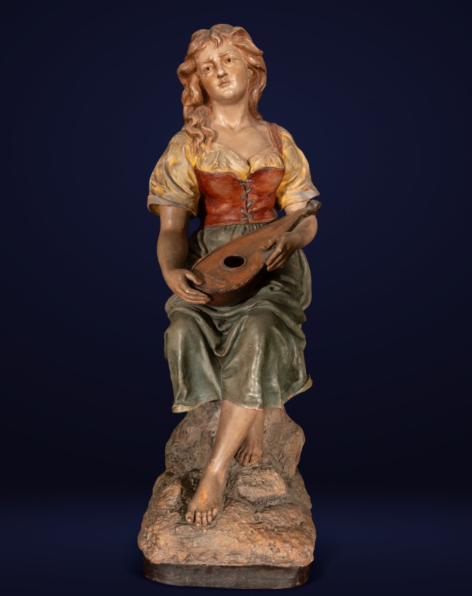 Lady with a Mandolin. French School. Signed J. Legeluche. 19th Century.: Polychrome terracotta sculpture. The work depicts a young woman seated on a rock formation, holding a mandolin in a contemplative attitude. With loose hair and a melancholic expression, she wears a ye