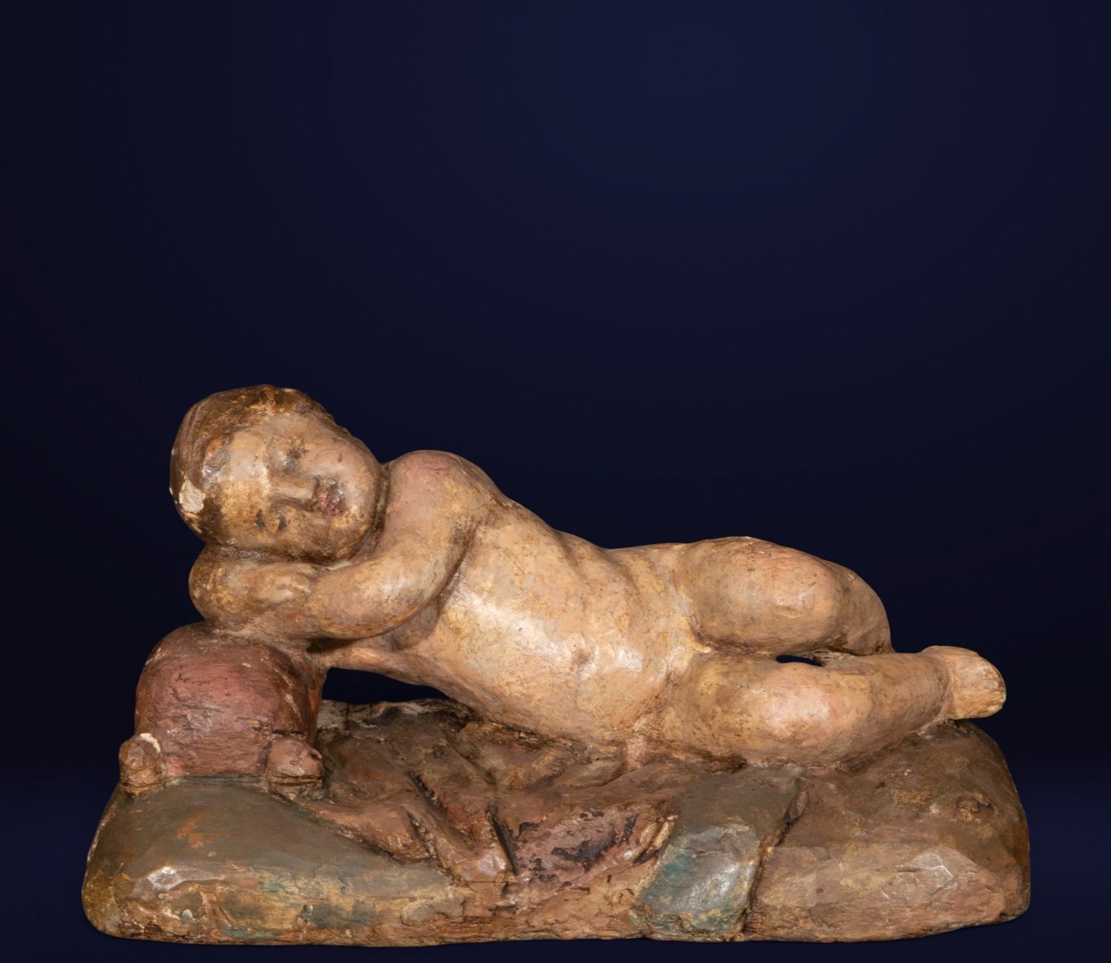 Sleeping Child Jesus, Spanish Baroque School, 17th Century: Polychrome wood carving. Measures 15 x 30 x 11 cm. Delicate representation of the Christ Child reclining on rocky ground, resting his head on one arm in a profound state of repose. The composition con