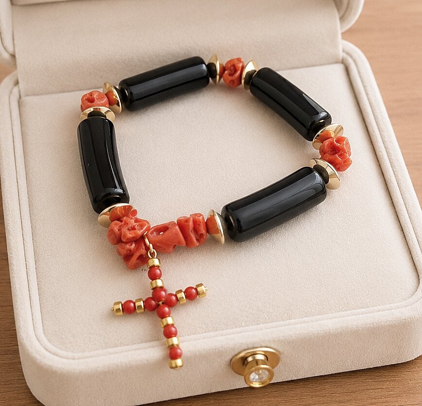 Bracelet with a hanging cross. Red coral, ebonite, and gilt-plated silver. Torre del Greco. 20th: Natural red coral, polished black ebonite, gold and silver-plated details. Adjustable size; cross 3 x 1 cm. Vintage bracelet made with alternating pieces of natural coral and cylindrical elements of p