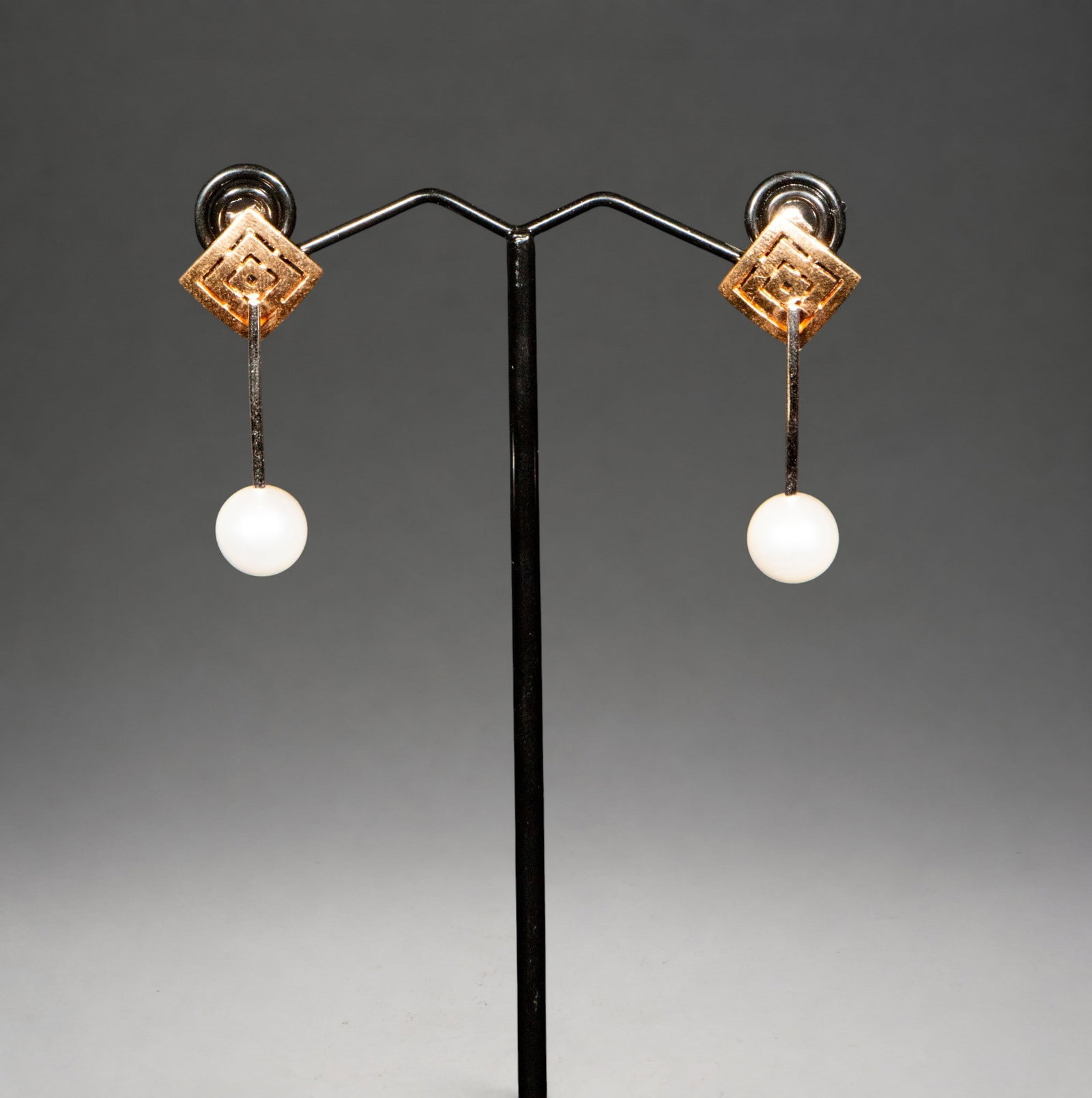 Two-tone earrings with a 9.5 mm cultured pearl. Weight 4 g.: Pair of earrings crafted in two-tone gold with a contemporary geometric design. The upper section features a rhomboid-shaped plate decorated with engraved concentric motifs, from which a spherical cul