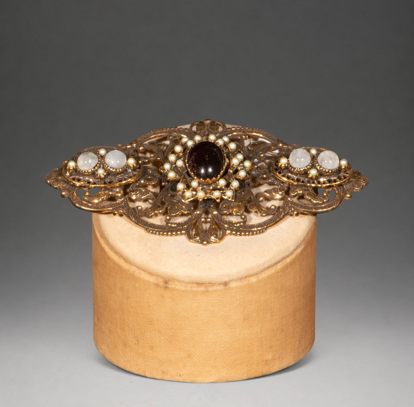 Gilded silver brooch with garnets and pearls: A gilt silver brooch in a historicist style with elaborate openwork filigree, decorated with a central garnet cabochon surrounded by small pearls and finished at the ends with clear cabochons and pear