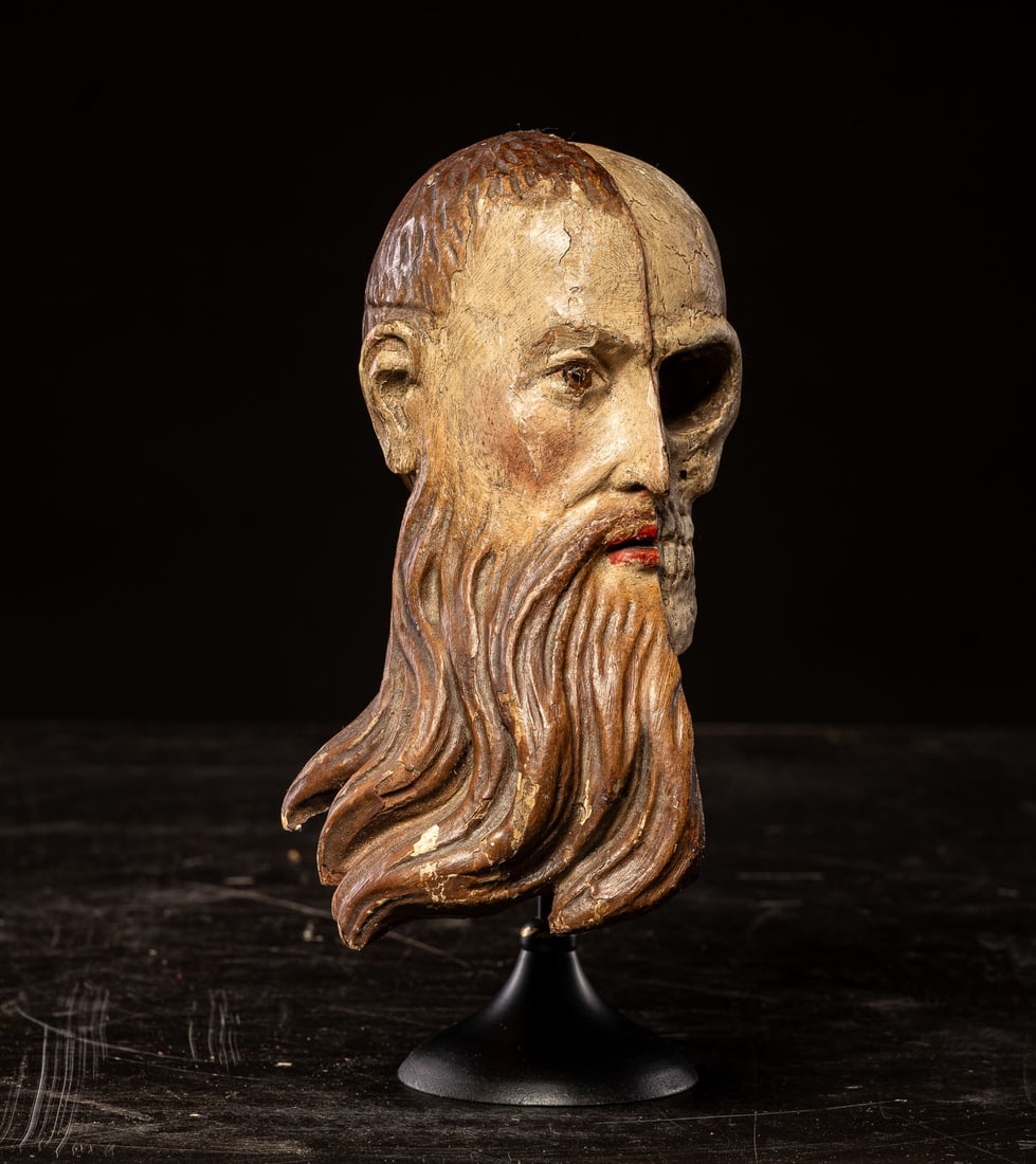 Small polychrome memento mori head, Europe, 19th century: Carved and polychromed wood. Dimensions: 23 x 11 x 11 cm. A small sculpture of intense symbolic content, conceived within the traditional iconography of memento mori, here resolved by a head divided v