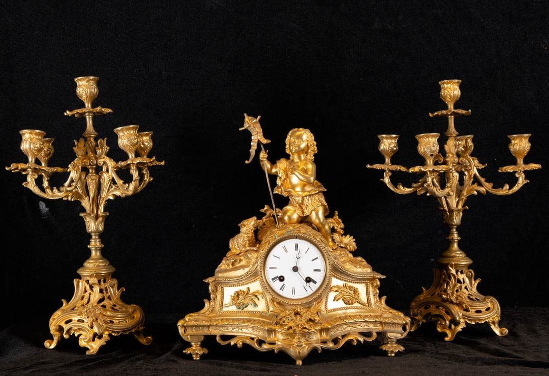 Complete French garniture in mercury-gilt bronze in the Louis XV style, 19th century French work: With Rocaille motifs and the figure of Saint John on the clock, working condition, clock measurements: 37 x 33 x 13 cm, candlestick measurements (each): 43 x 23 x 21 cm
