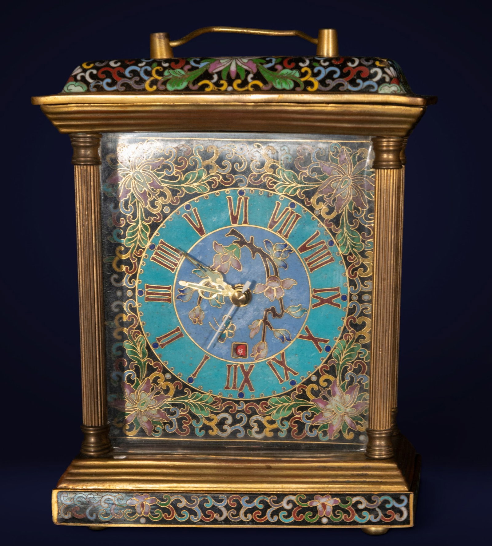 Claude alarm clock, French School, 20th century: Gilt metal and cloisonné enamel. Dimensions: 23 x 16 x 8 cm. Tabletop alarm clock with an architectural case decorated with polychrome enamels of floral motifs and a central dial with Roman numerals 