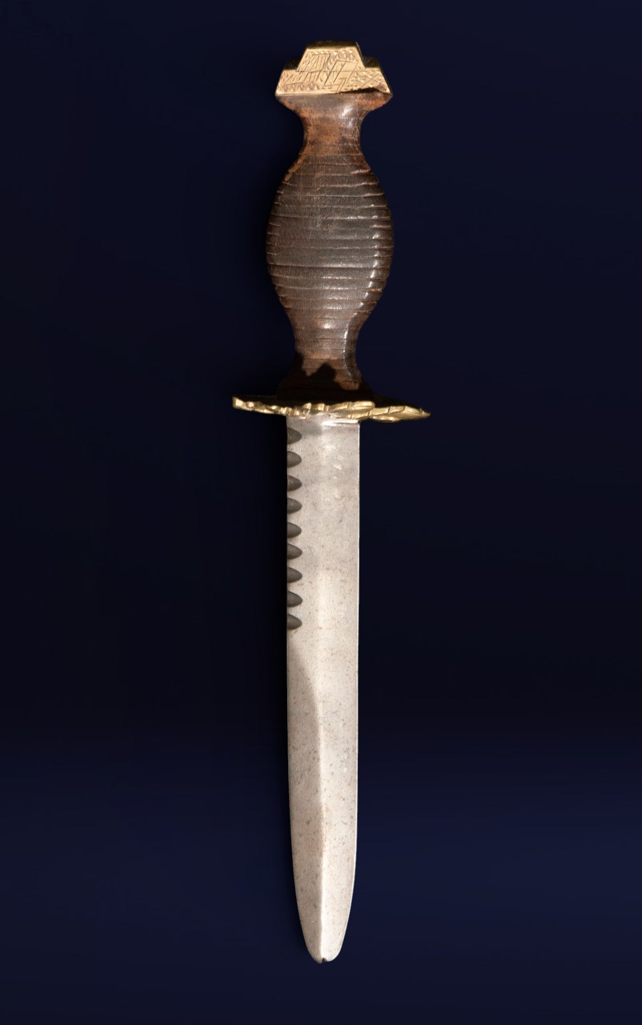 Dagger, Oriental School, 18th Century: Forged steel, wood, and gilt metal. Dimensions: 28 x 6 x 6 cm. A dagger with a straight, wide blade and a carved wooden hilt with a globular profile and metal fittings engraved with geometric motifs. 