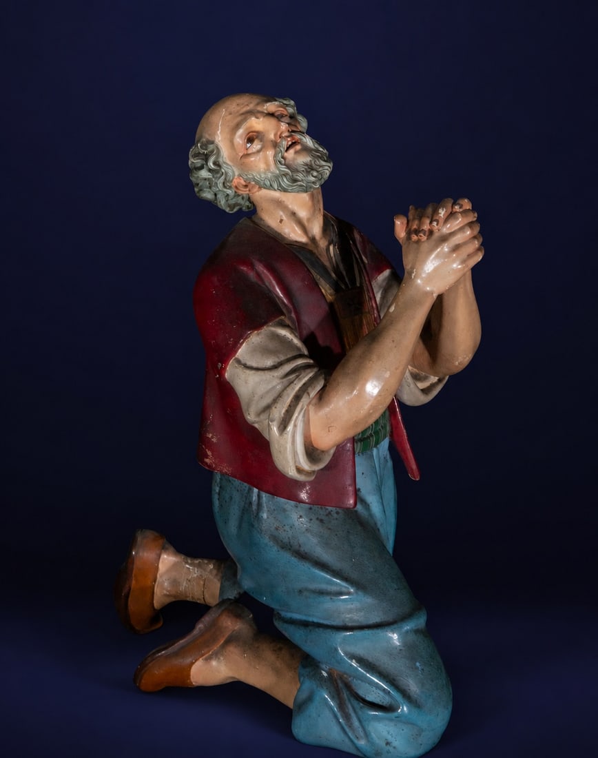 19th-century Neapolitan Nativity scene figure: Carved and polychromed sculpture. A male figure kneels in prayer, his hands clasped and his face raised towards heaven in a gesture of intense devotion. He wears a blue tunic and a reddish vest over a