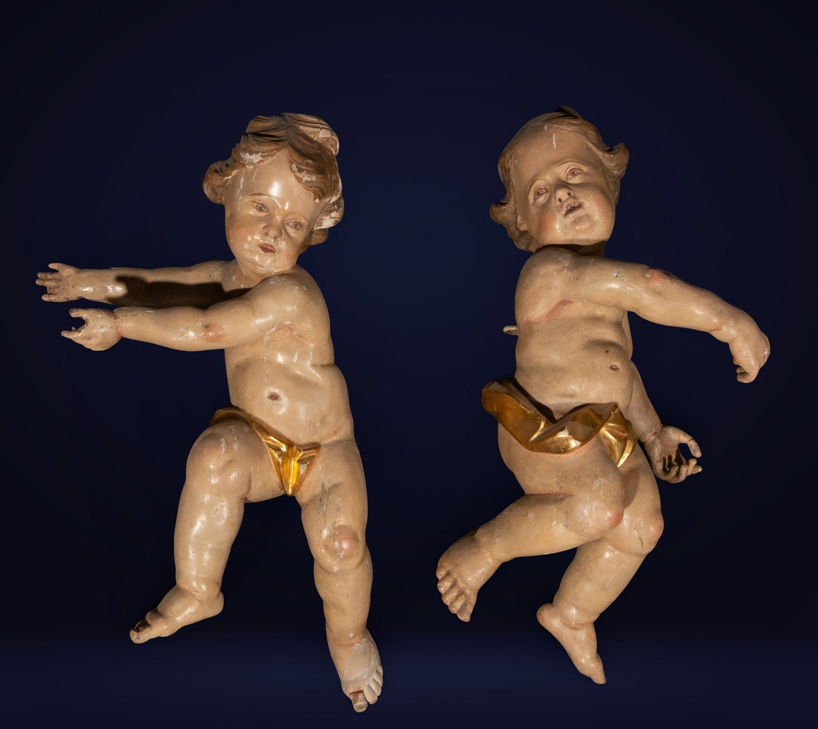 Pair of angels, Spanish School, late 18th and early 19th century: Carved, polychromed, and gilded wood. A pair of child angels depicted in a dynamic, suspended pose, with rounded anatomies and expressive gestures that convey a sense of upward movement. The polychrom