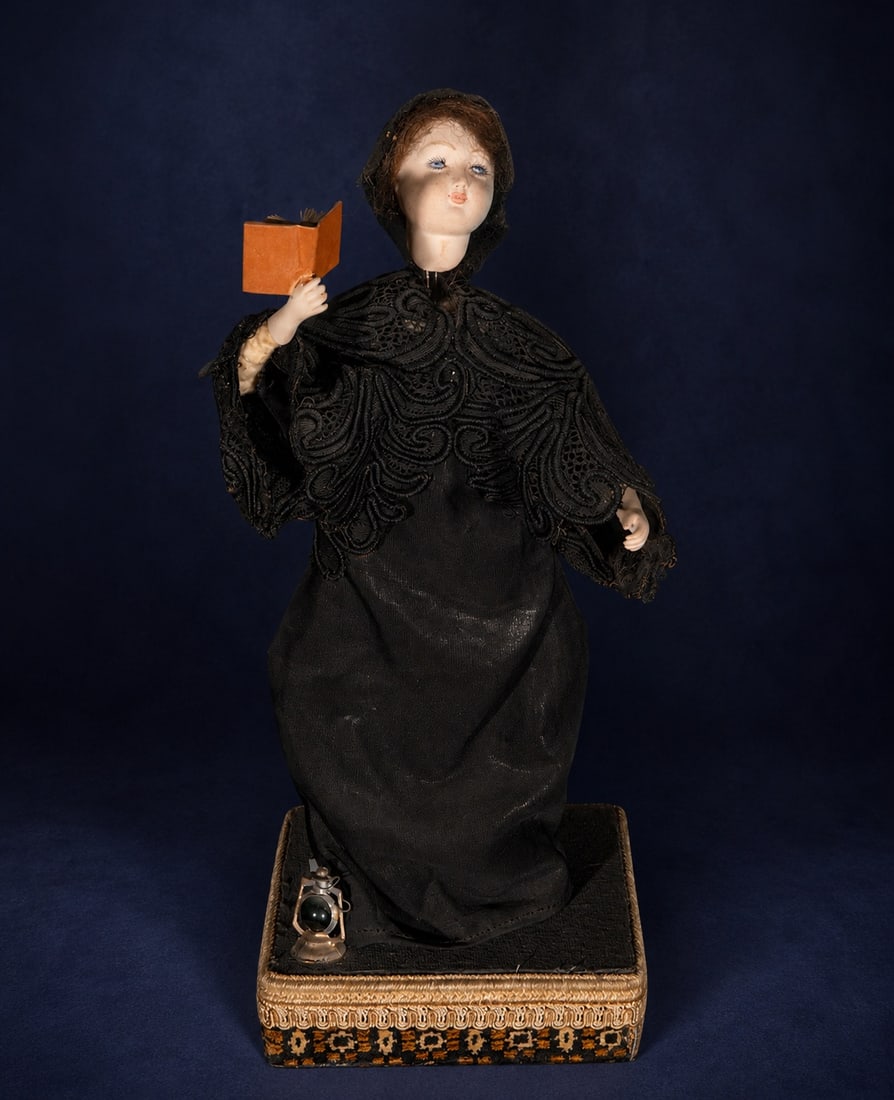 Automaton of a reader with a book, European school, 19th century: Automaton depicting a female figure dressed in black with elaborate Victorian-inspired lace, holding a small open book as if reading. The porcelain face, with its delicate features and upward gaze, co