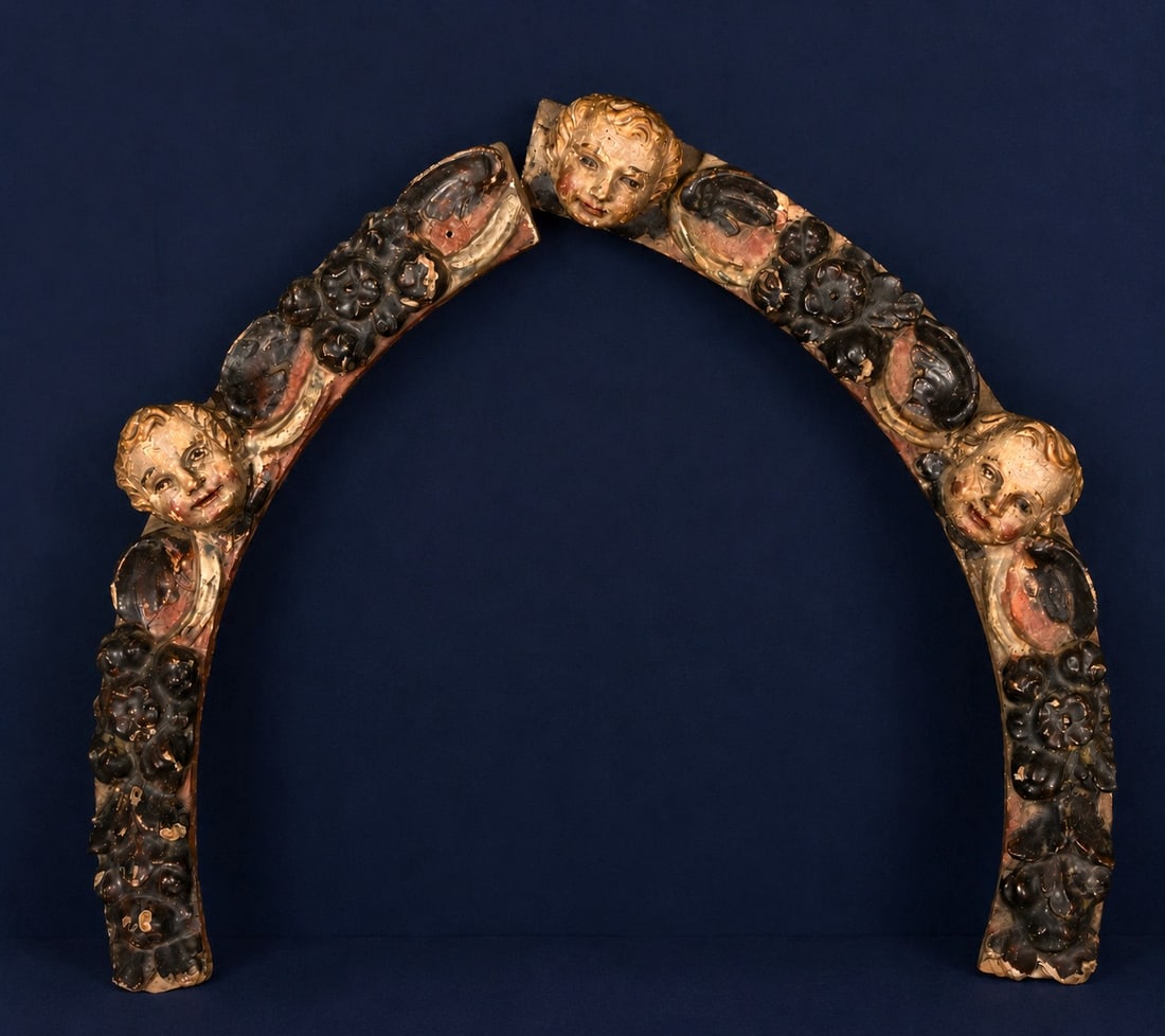 Oval finial with angel heads, Spanish School, 17th century: Carved and polychromed wood. Oval-shaped architectural finial decorated with cherub heads distributed along an arched structure covered with vegetal and floral motifs in relief. The composition displa