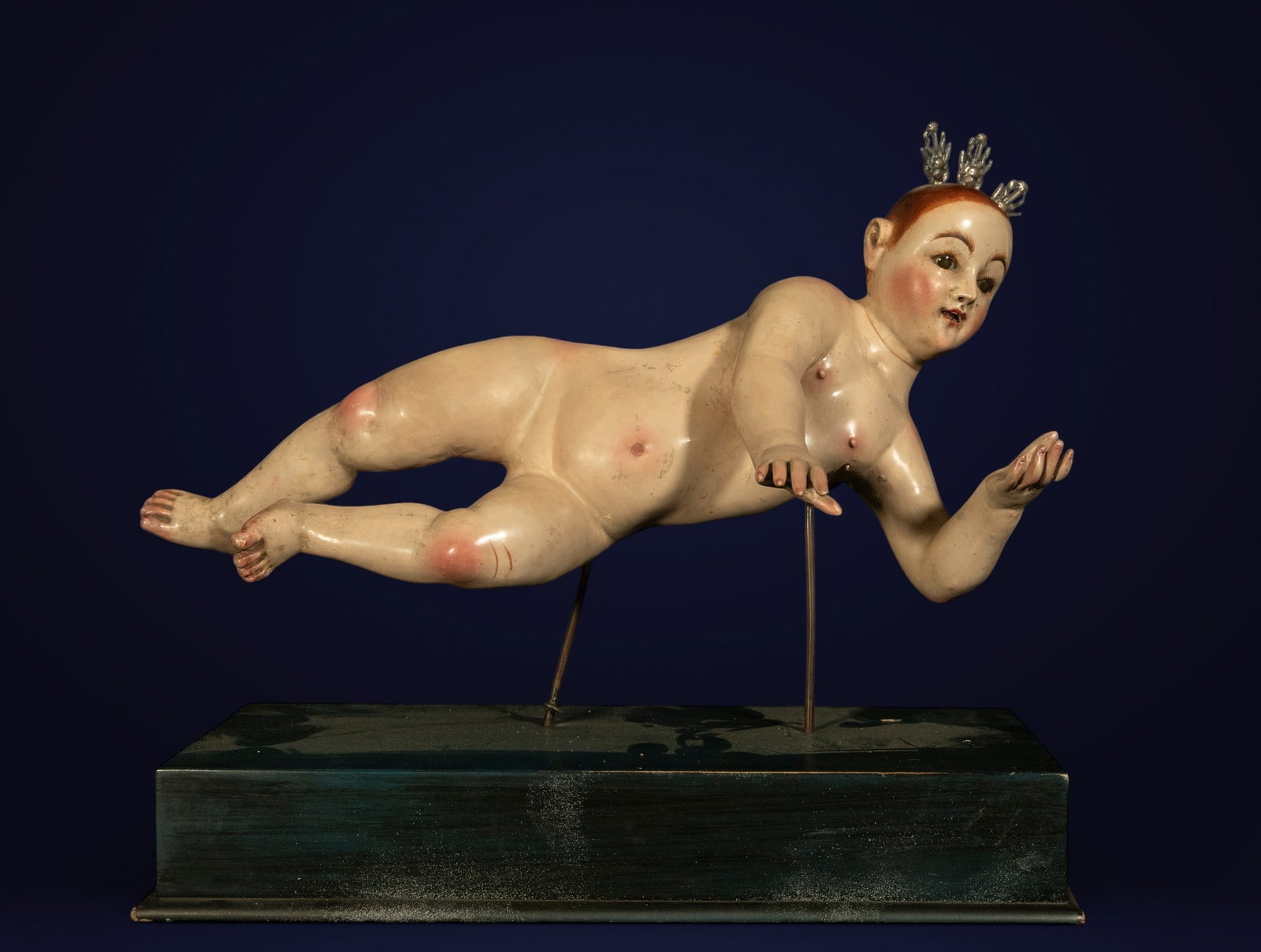 CAPISCARA CIRCLE. QUITO COLONIAL SCHOOL, ECUADOR, 18TH CENTURY - Triumphant Child Jesus: Carved and polychromed wood sculpture with silver rays. Dimensions: 16 x 30 x 13 cm. The sculpture depicts the nude Christ Child in a triumphant and ascending pose, with his head slightly turned and o