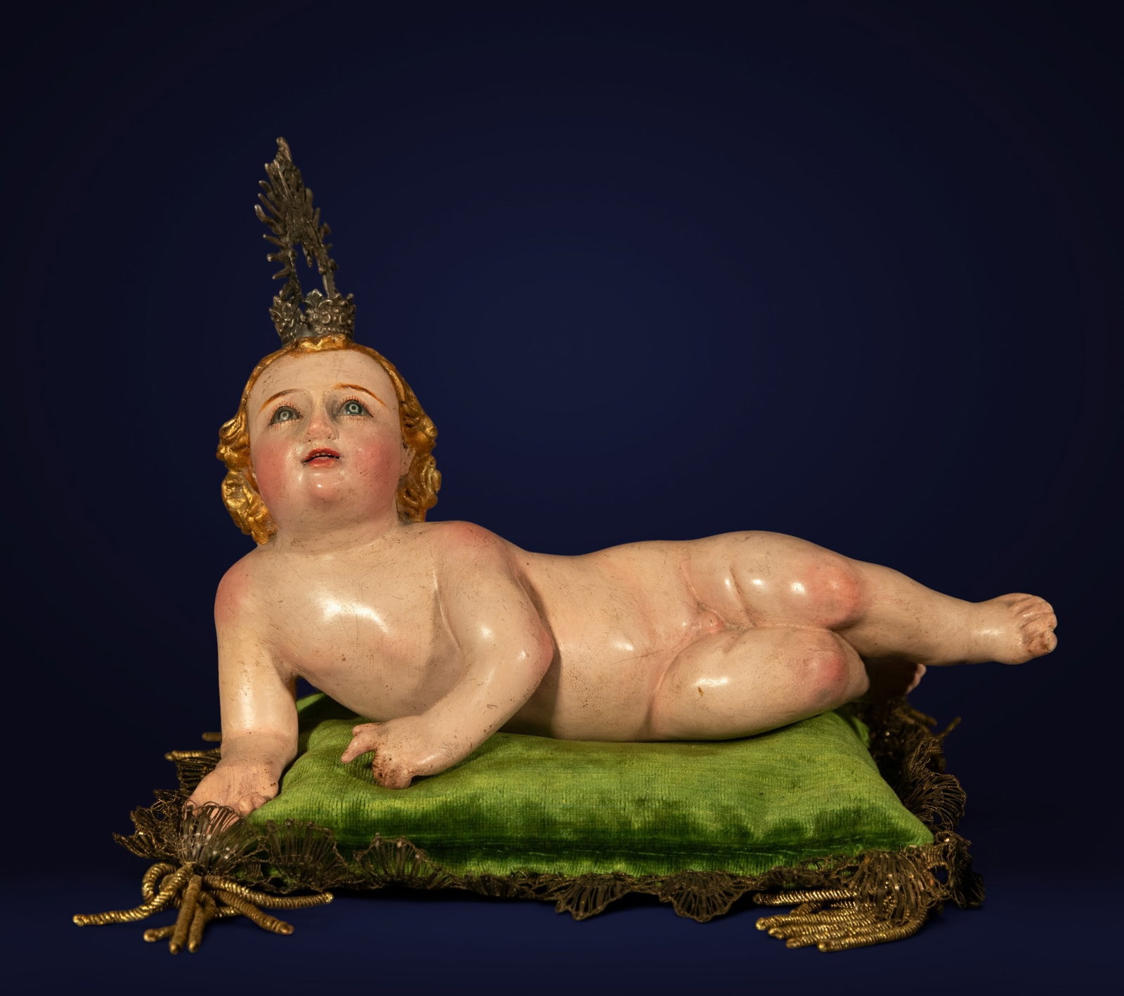 CASPICARA CIRCLE. QUITO SCHOOL, ECUADOR, 19TH CENTURY - Reclining Child Jesus: Carved and polychromed wood figure with a silver crown. Includes a period embroidered cushion. Dimensions: 13 x 23 x 8 cm. Delicate representation of the Christ Child reclining on a green velvet cushi