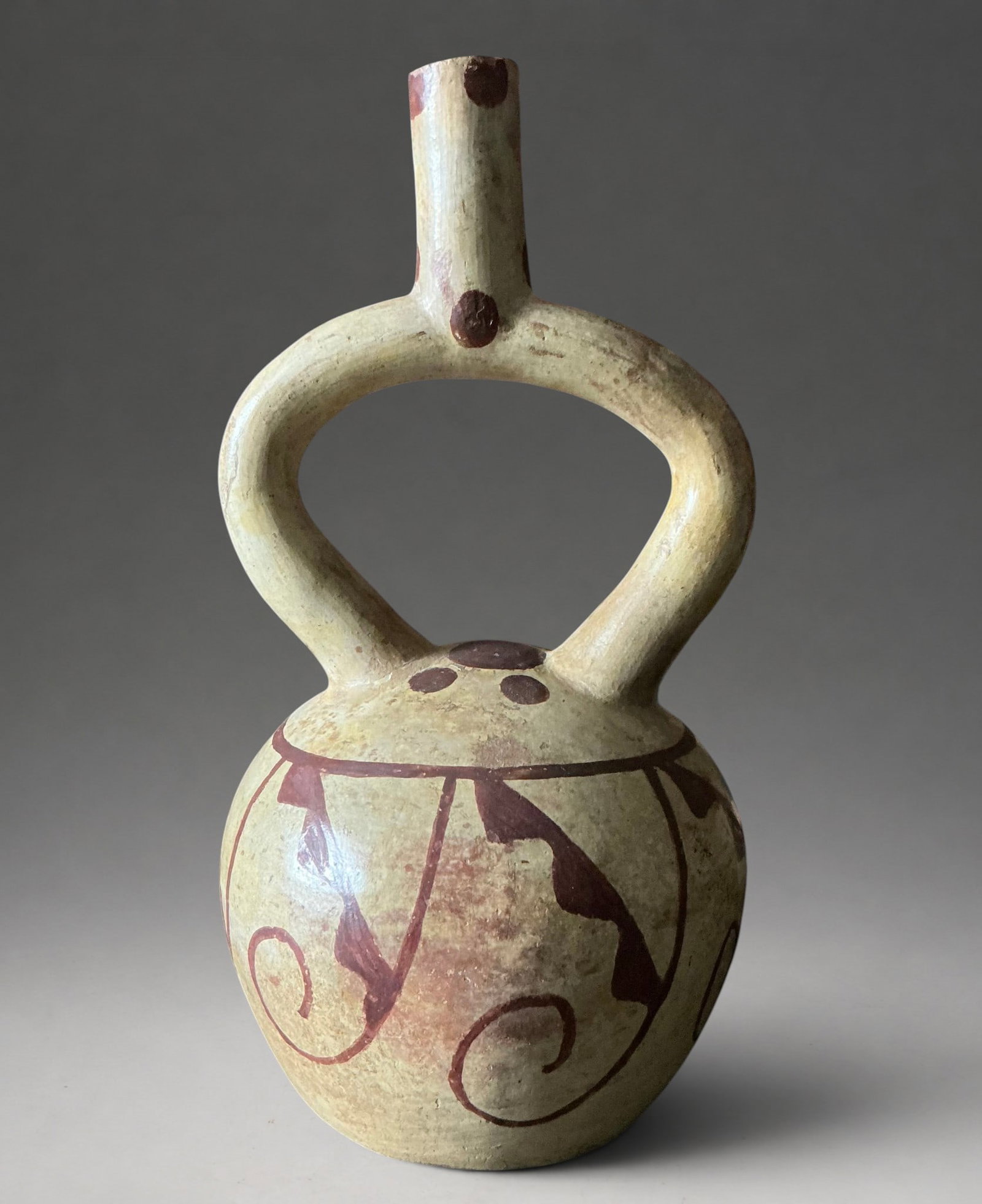 Stirrup vessel with geometric decoration, Moche Culture, 200-800 AD: Modeled and painted ceramic. Measures 27.3 cm in height. Pre-Columbian vessel with a globular body, stirrup handle, and tubular spout, decorated with geometric motifs and sinuous lines in reddish pigm