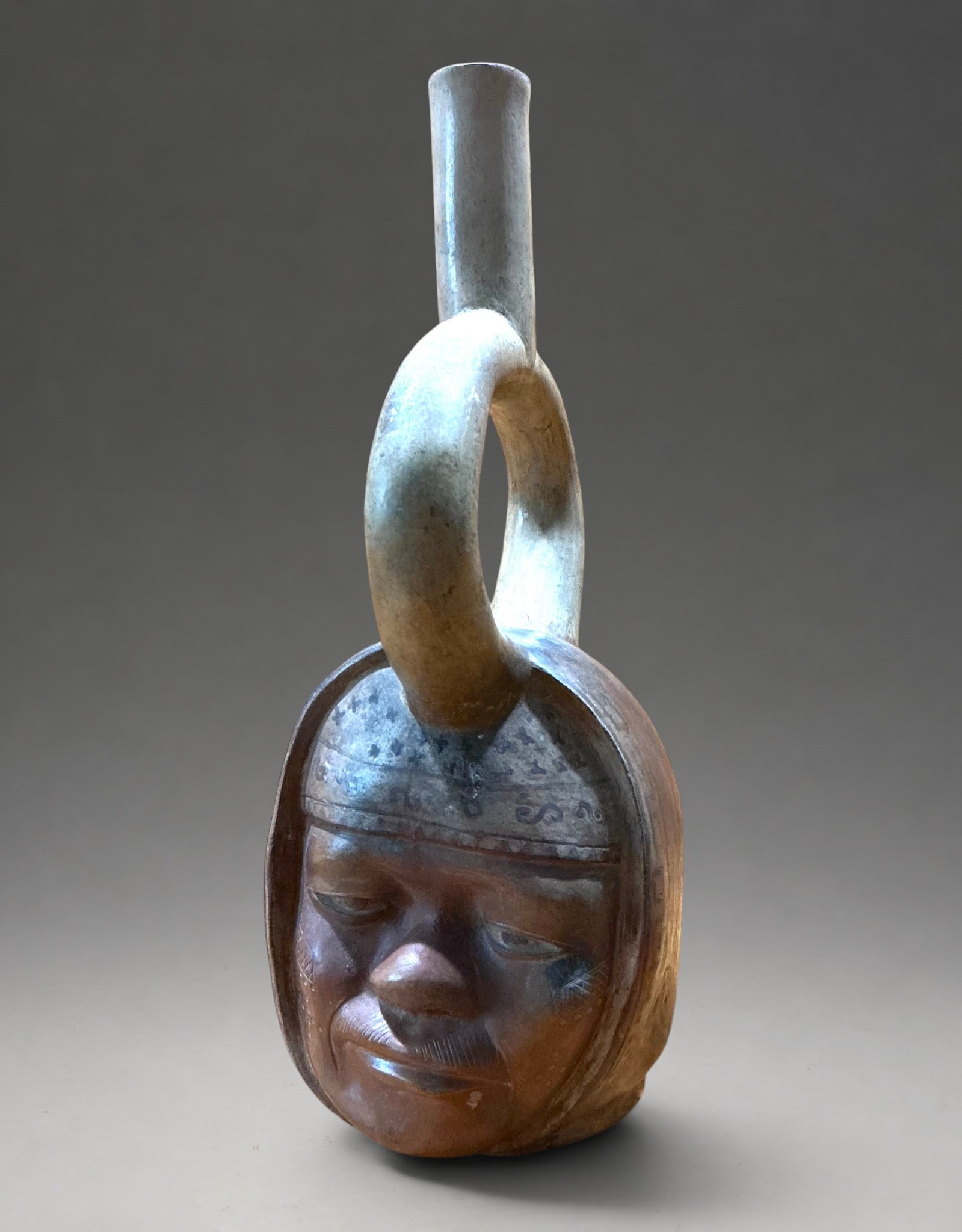 Anthropomorphic stirrup-shaped portrait vessel, Moche Culture, 600-800 AD: Modeled ceramic with a male anthropomorphic representation and a tubular handle. Pre-Columbian vessel with a sculpted body depicting a seated human figure with voluminous limbs and a head with schemat