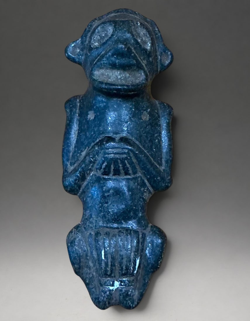 Dominican Zemi amulet or anthropomorphic Cemí, Taíno Culture, 11th-15th centuries: Polished hard stone. Measures 10.5 cm. Small Taíno amulet with a stylized anthropomorphic figure and schematic facial features carved in relief. The piece has perforations and a gently polished surfa