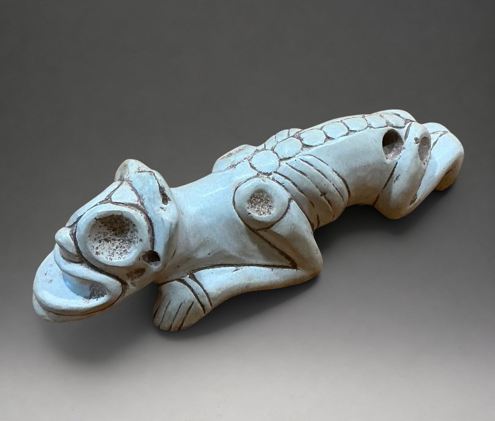 Zemi or Cemí amulet, shamanic, Dominican Republic, Taíno culture, 11th-15th centuries: Polished and incised hard stone. Measures 12 cm. Taíno ceremonial amulet with a reclining zoomorphic figure with an elongated body and flexed limbs. The head has a perforated tubular mouth and deeply