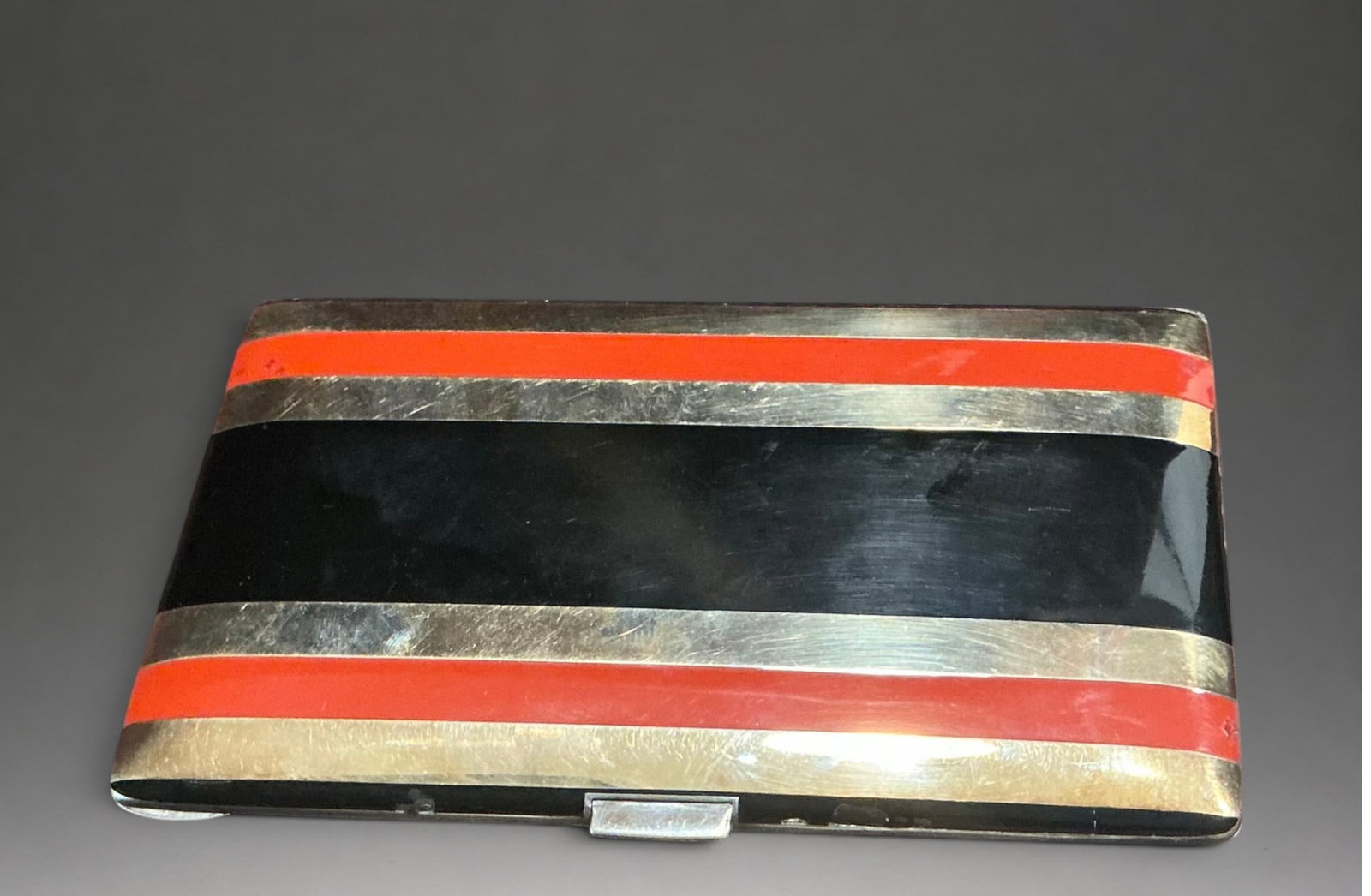 Art Deco enameled cigarette case, United States, 20th century: Gilded silver with black and red enamel and 14-karat gold accents. Measures 13.2 x 8.4 cm. Weight 172.3 grams. Rectangular cigarette case with geometric lines decorated with alternating horizontal str