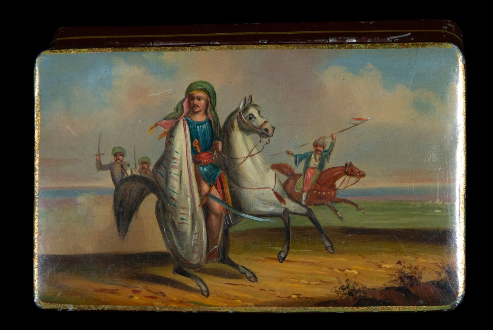 Enameled box painted with equestrian scene, Orientalist School, 19th Century: Lacquered and painted metal. Dimensions: 3 cm x 13 cm x 8 cm. Rectangular box decorated with an Orientalist scene featuring armed horsemen against an open landscape. The composition is notable for the