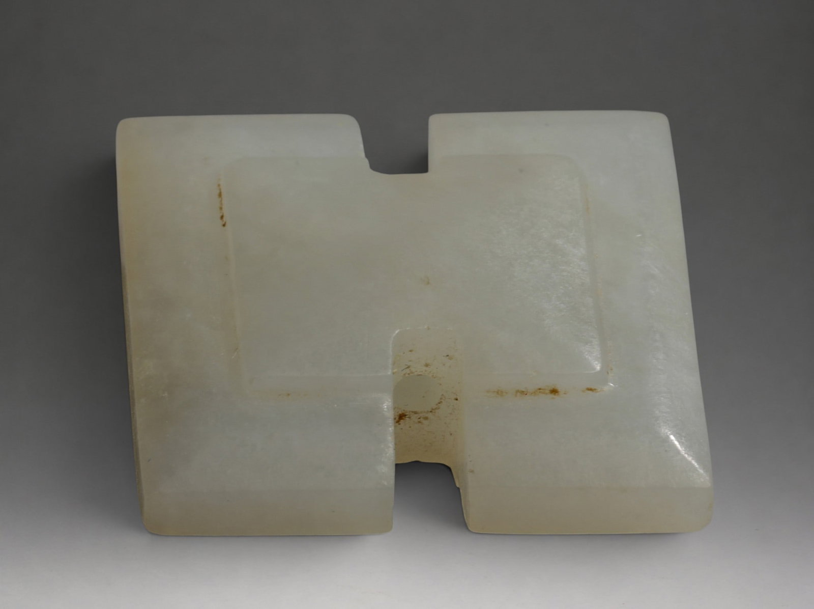 Rare Jade Quadrangular Ornament Element, Han Dynasty, 2nd Century BC - 3rd Century AD: Carved white celadon jade. Dimensions not indicated. Quadrangular piece with a double notch and a central circular perforation. The surface has a smooth finish and a translucent white tone with slight